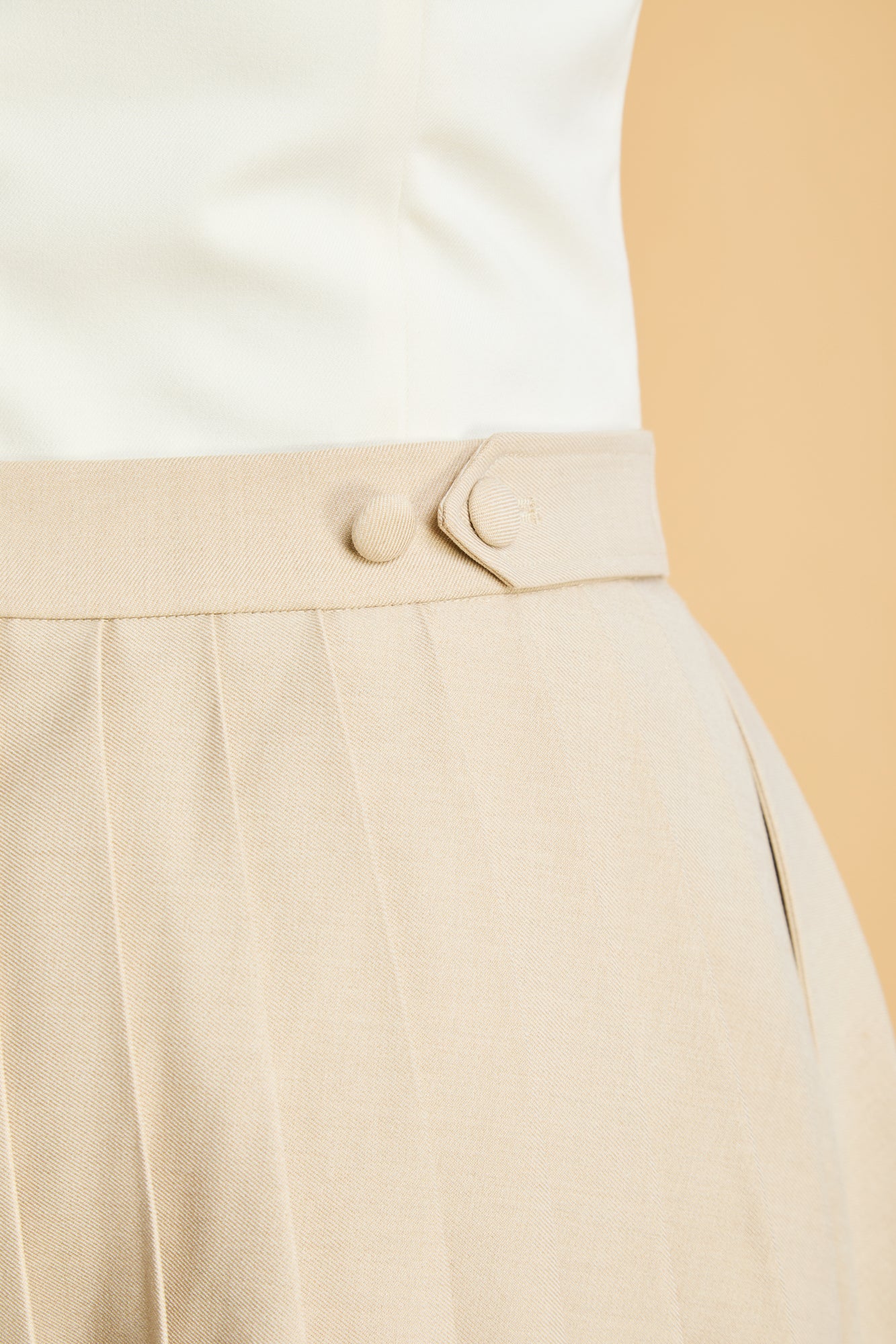 close up of the adjustable double button tab on waist of the Triplicity pleated mini skirt