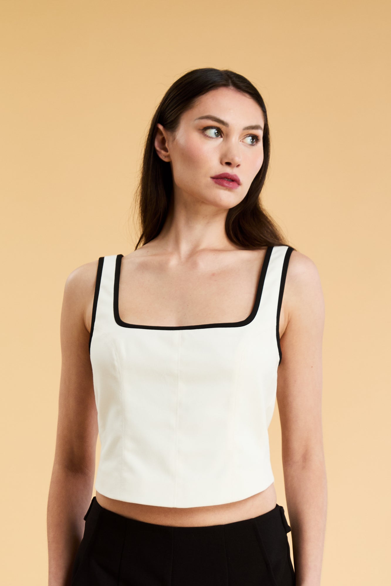 Person wearing a White Triplicity Eloise sleeveless tank top and Black Adelaide pants on a beige background front view close up