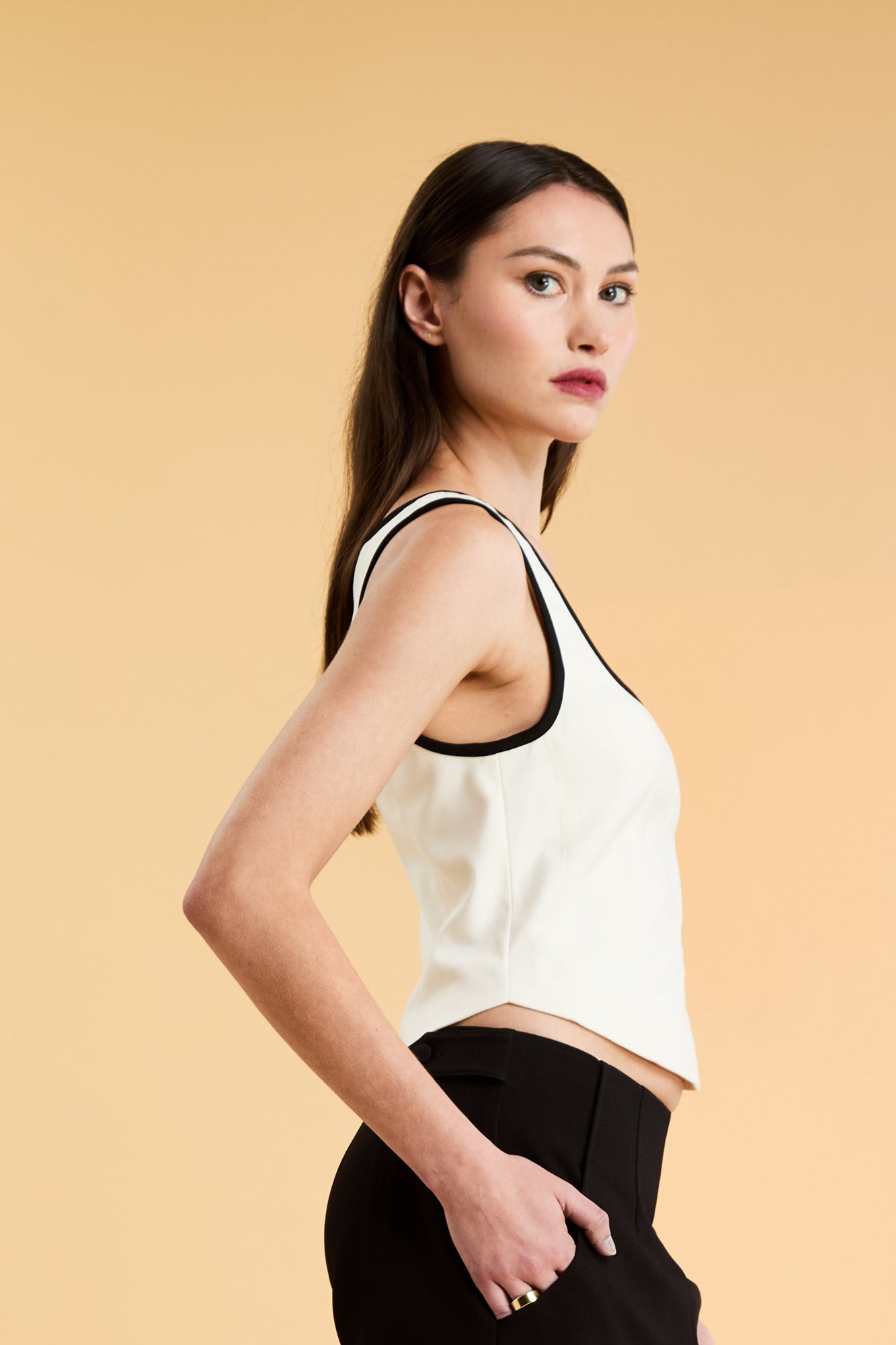 Person wearing a White Triplicity Eloise sleeveless tank top and Black Adelaide pants on a beige background side view close up