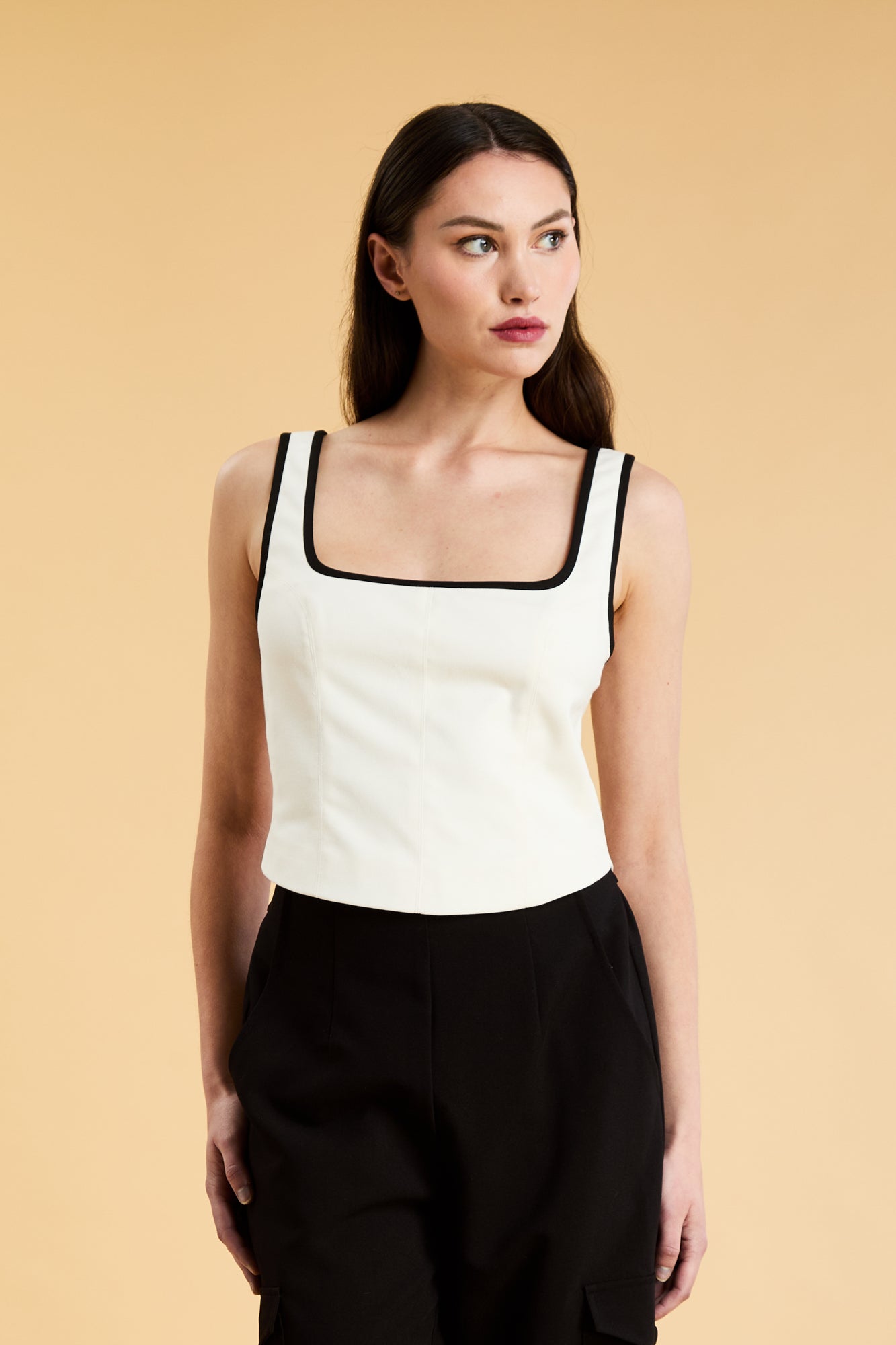 Person wearing a White Triplicity Eloise sleeveless tank top and Black Adelaide pants on a beige background front view close up