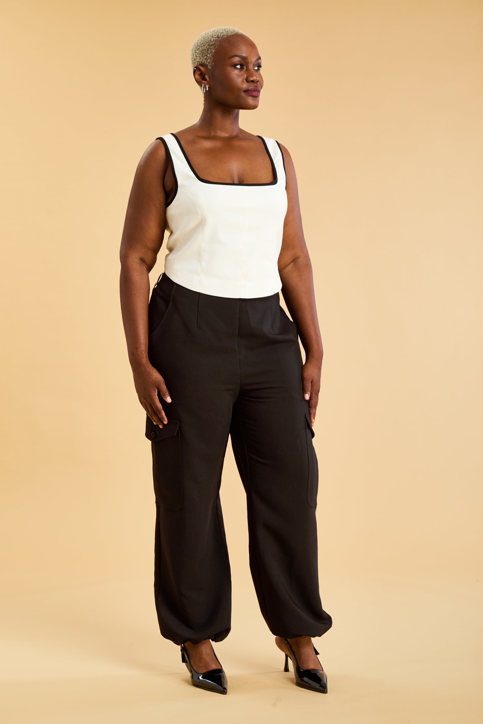 Person wearing a White Triplicity Eloise sleeveless tank top and Black Adelaide pants on a beige background front view full body