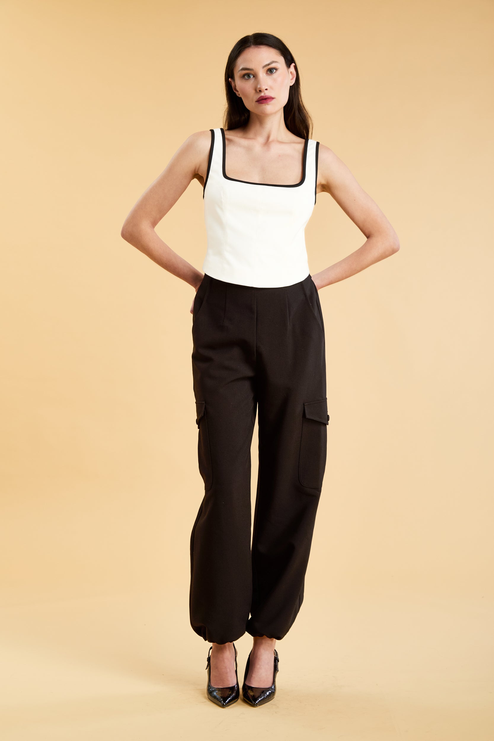 Person wearing a White Triplicity Eloise sleeveless tank top and Black Adelaide pants on a beige background front view full body