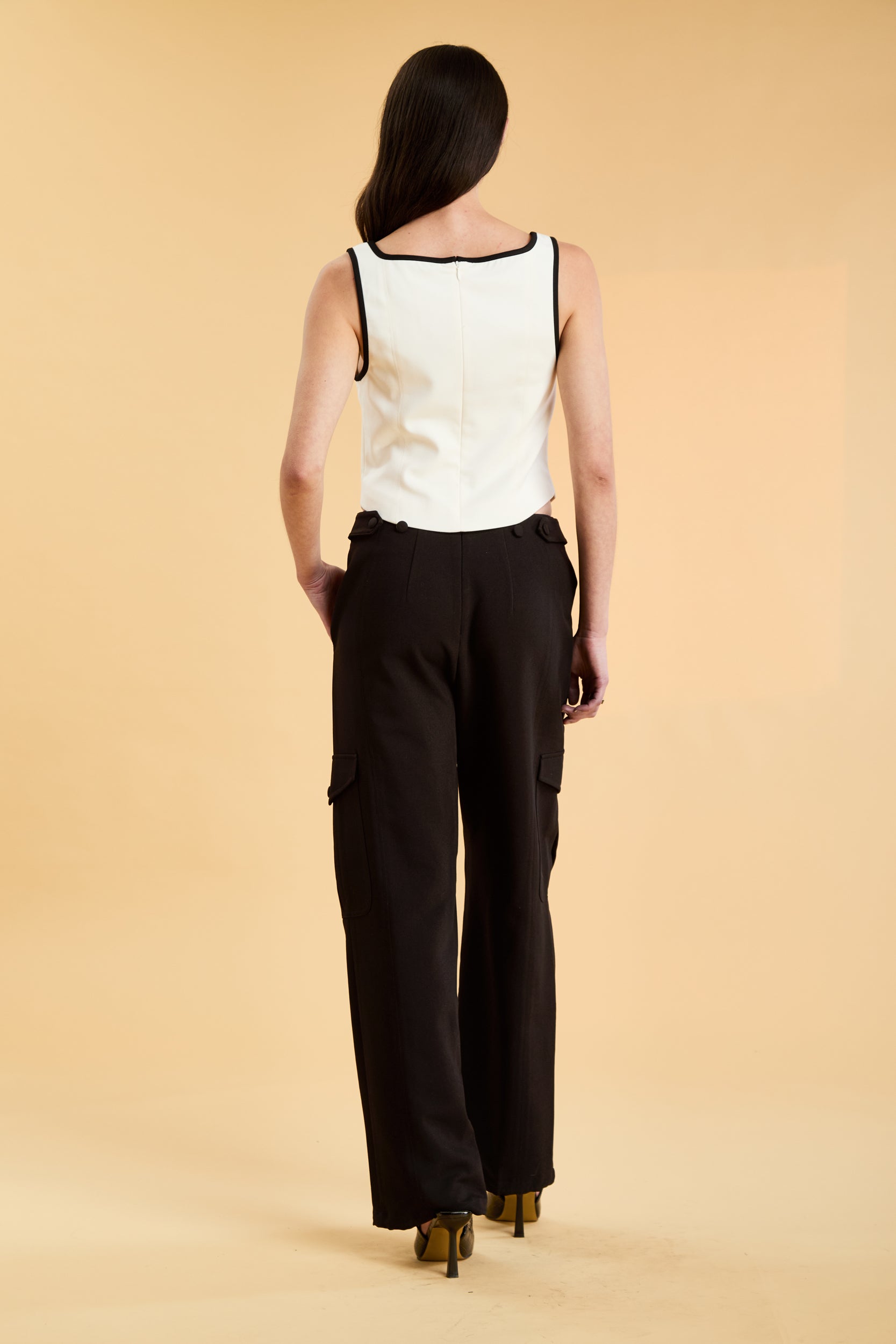 Person wearing a White Triplicity Eloise sleeveless tank top and Black Adelaide pants on a beige background back view full body