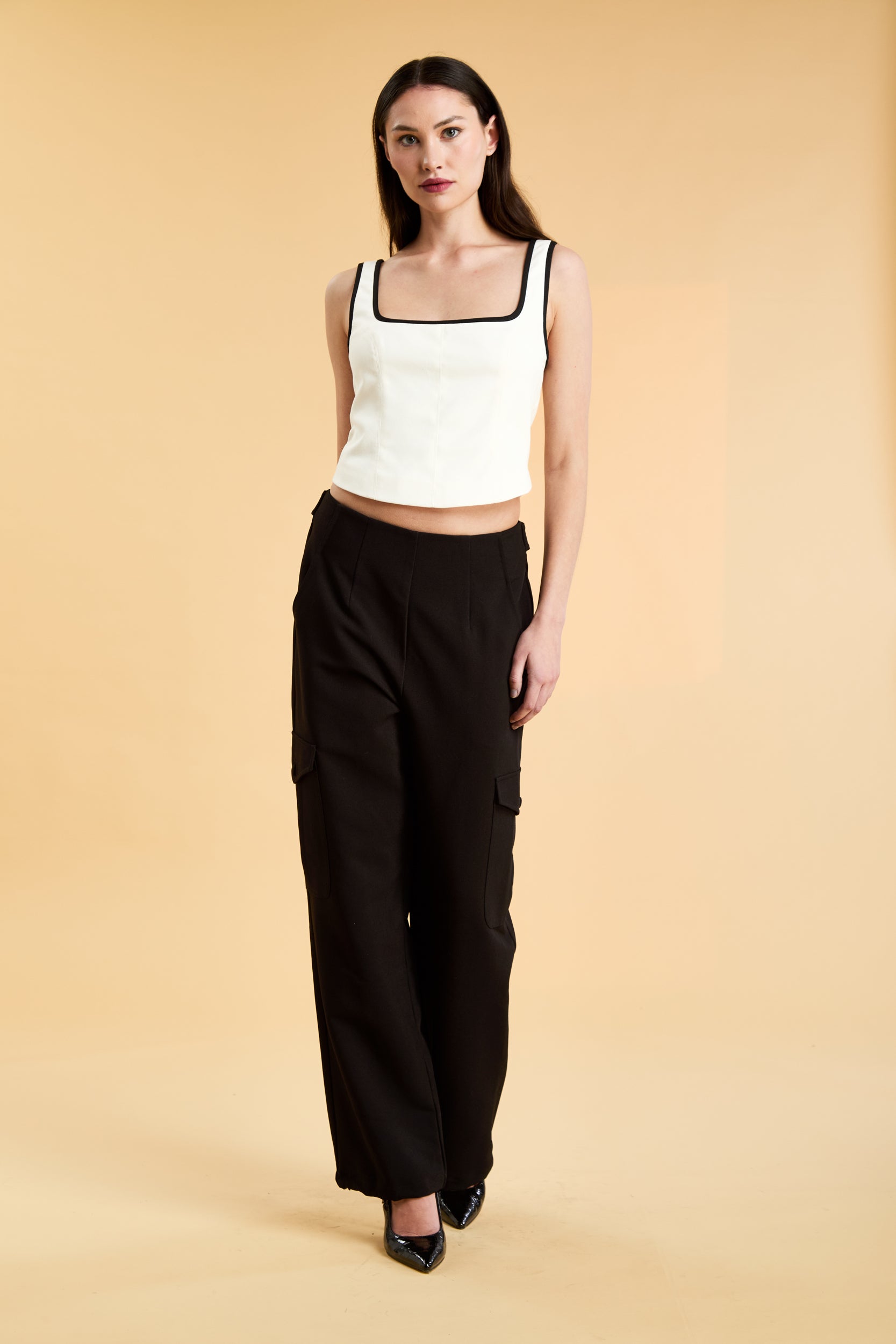 Person wearing a White Triplicity Eloise sleeveless tank top and Black Adelaide pants on a beige background front view full body