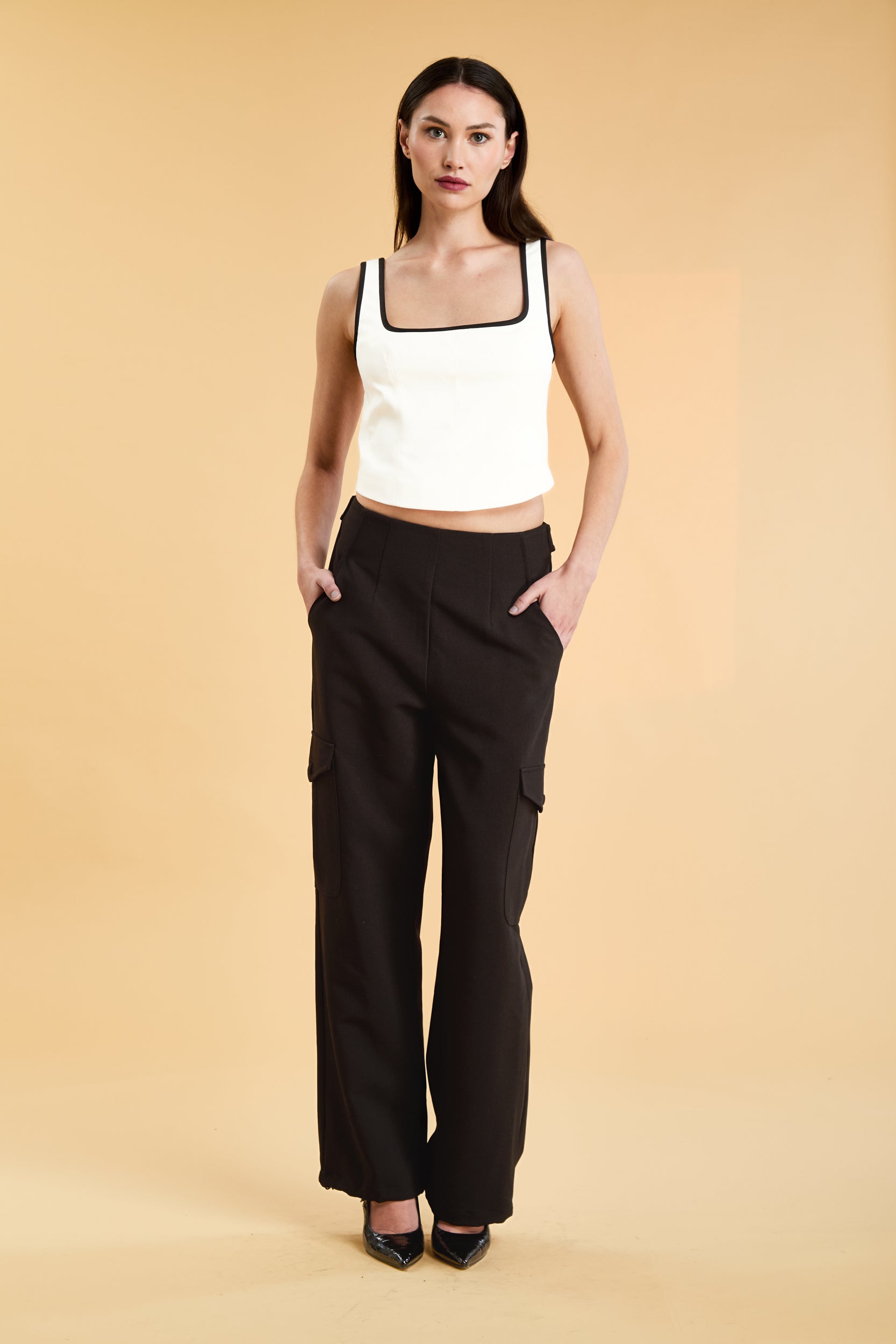 Person wearing a White Triplicity Eloise sleeveless tank top and Black Adelaide pants on a beige background front view full body