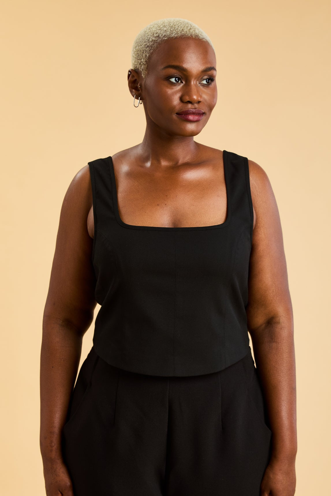 Woman wearing a Black Triplicity sleeveless Eloise tank up against a beige background front view close up