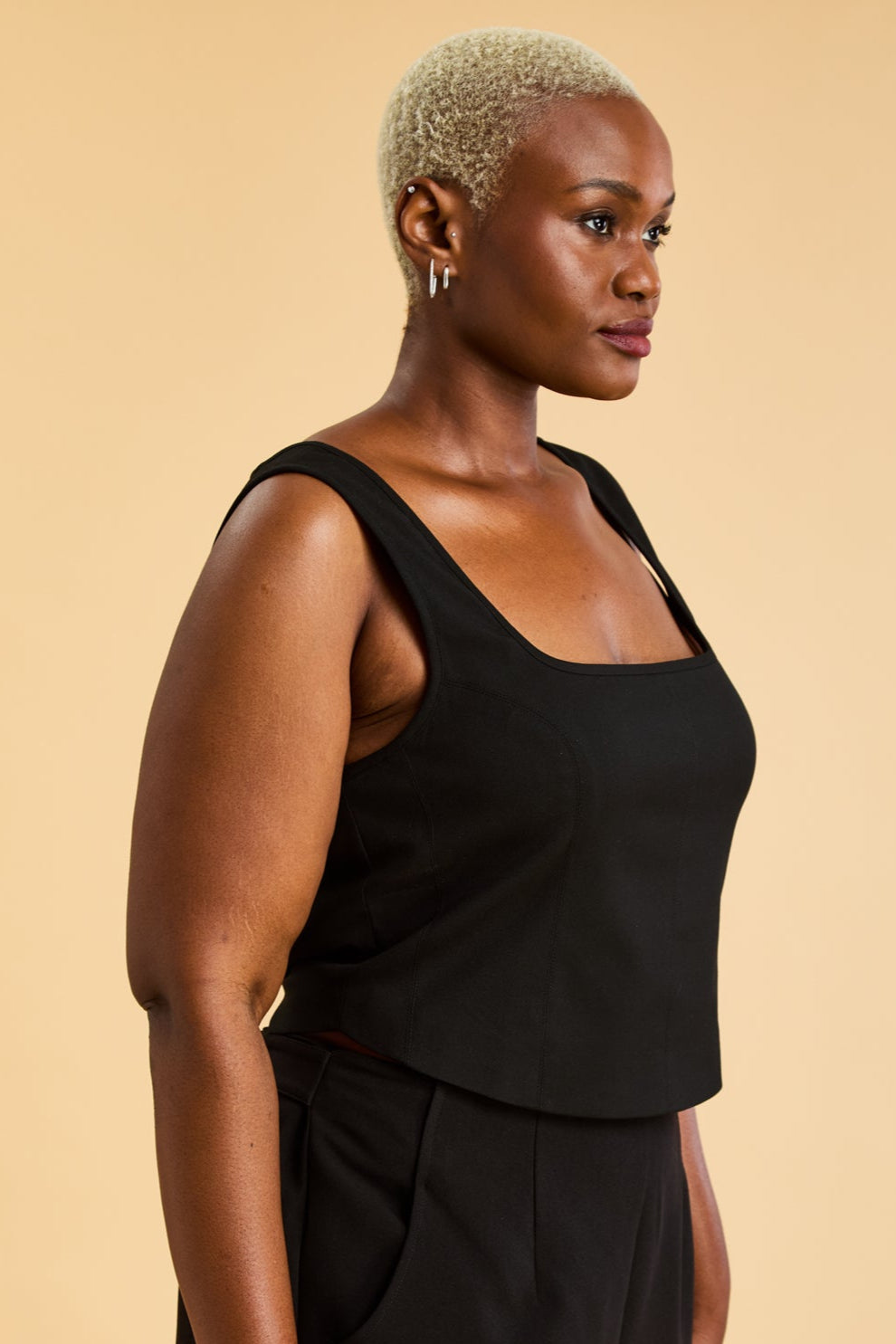 Woman wearing a Black Triplicity sleeveless Eloise tank up against a beige background front view close up