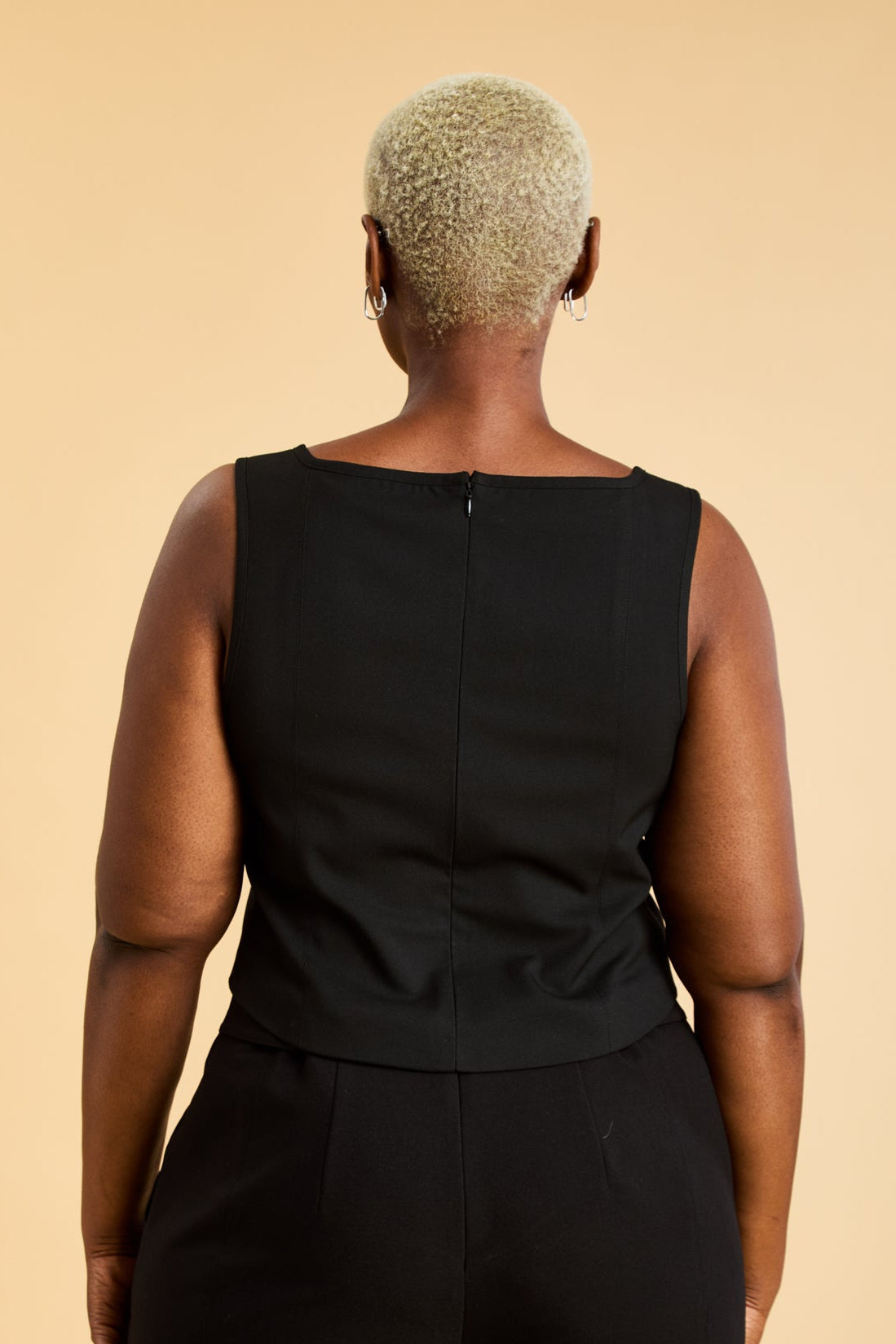 Woman wearing a Black Triplicity sleeveless Eloise tank up against a beige background back view close up