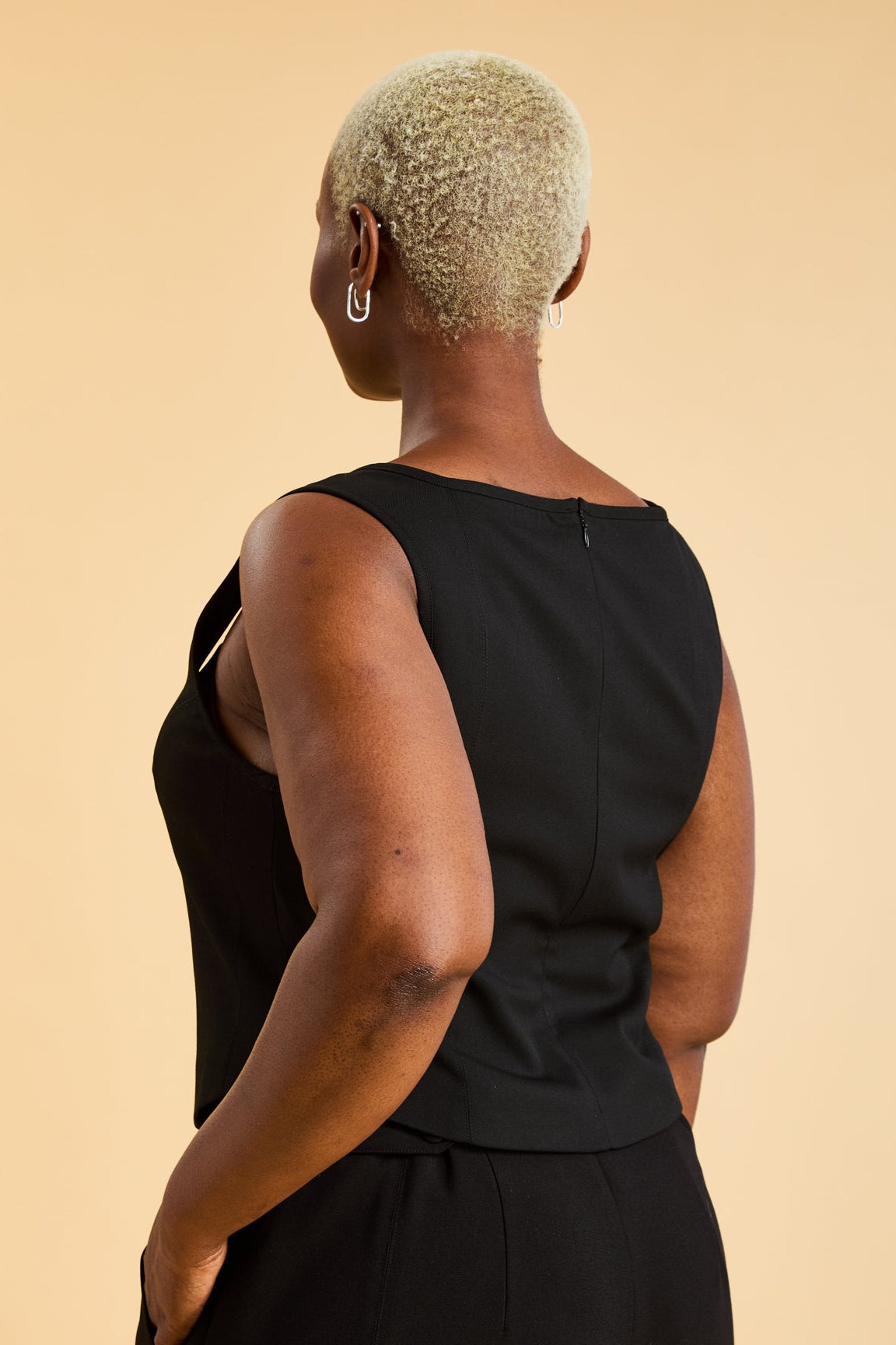 Woman wearing a Black Triplicity sleeveless Eloise tank up against a beige background back view close up