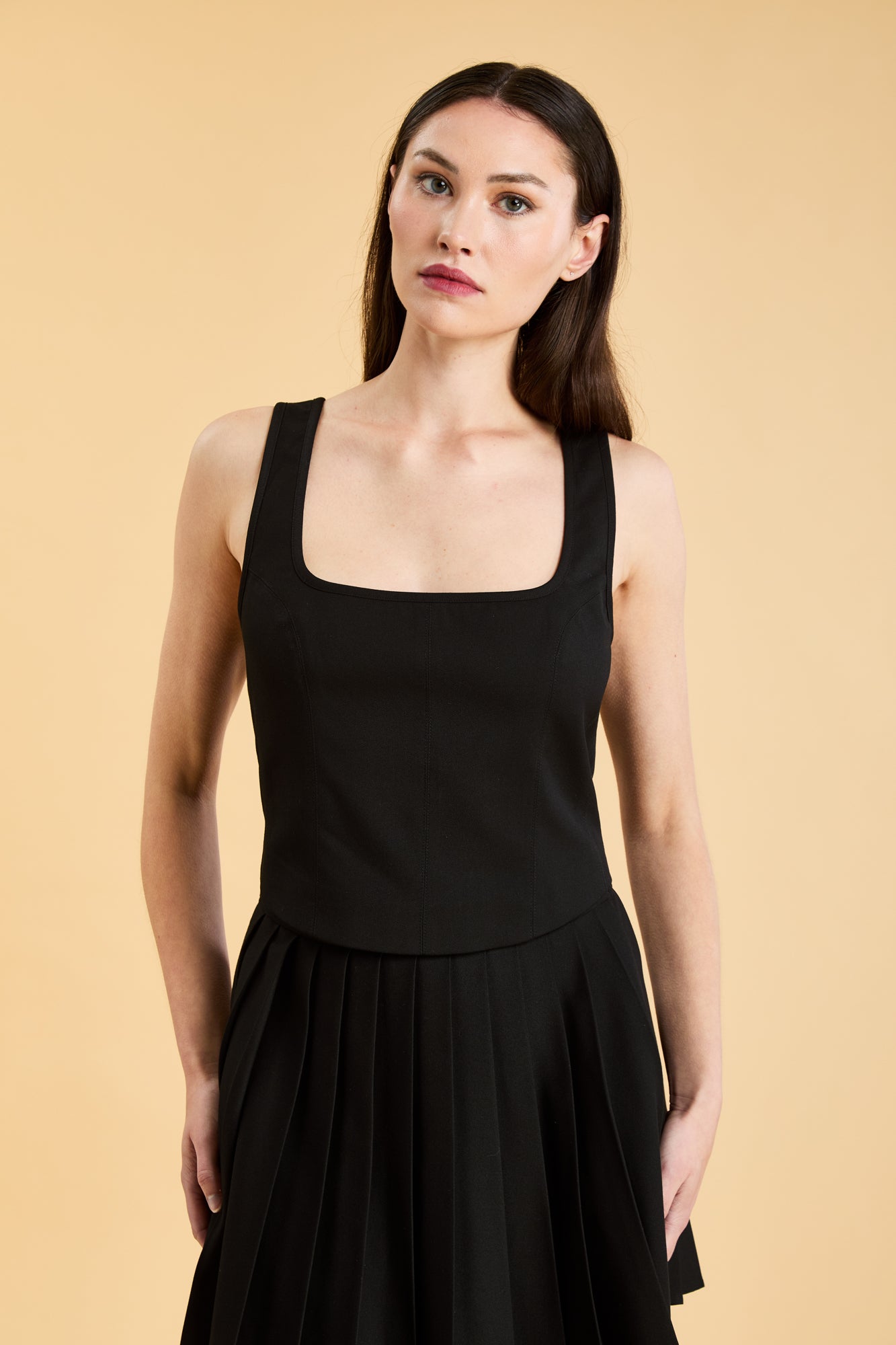 Woman wearing a Black Triplicity sleeveless Eloise tank up against a beige background front view close up