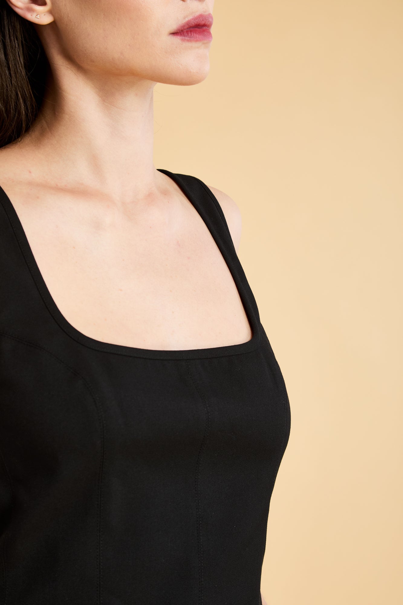 Woman wearing a Black Triplicity sleeveless Eloise tank up against a beige background front view close up