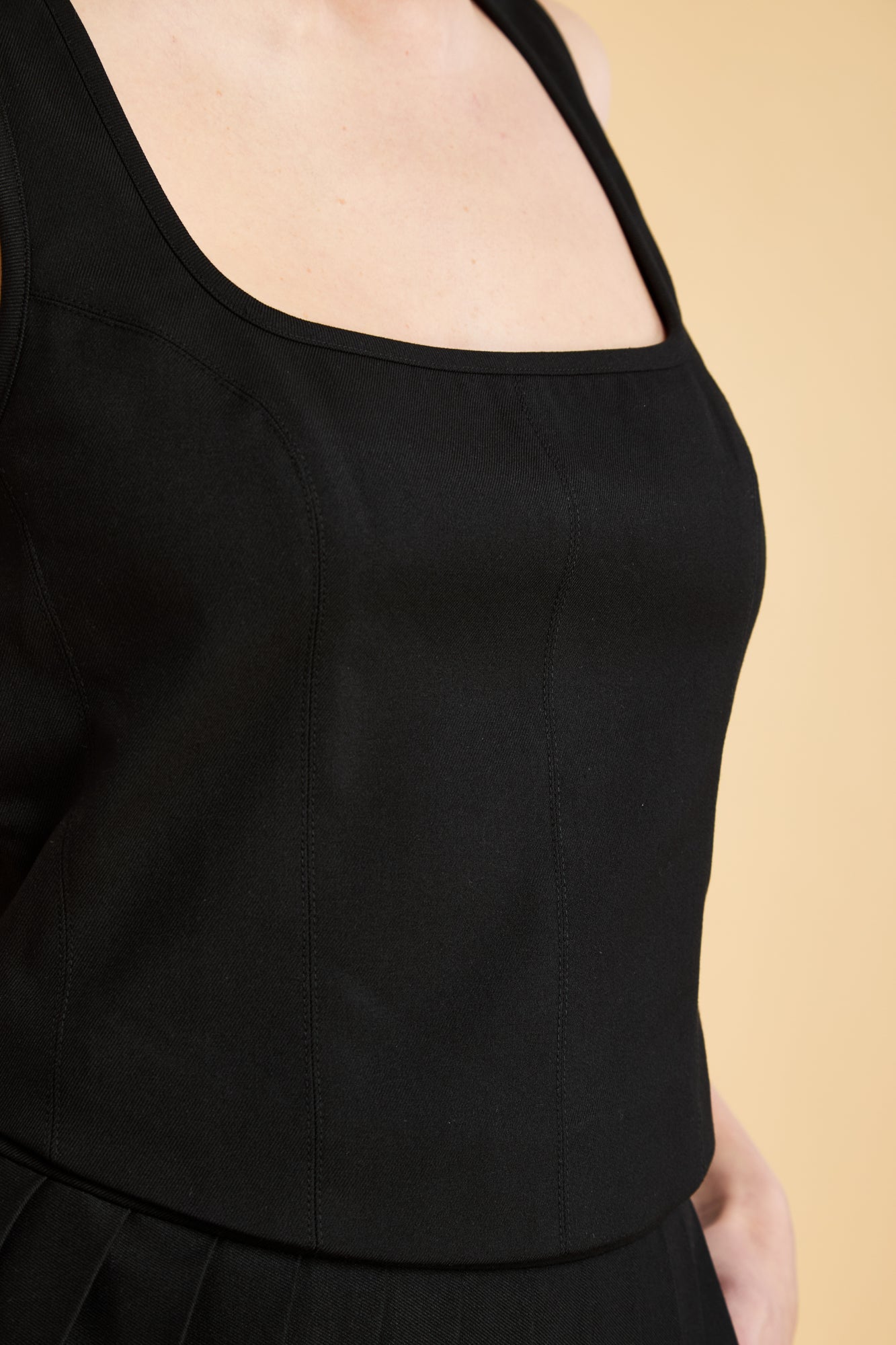 Woman wearing a Black Triplicity sleeveless Eloise tank up against a beige background front view close up