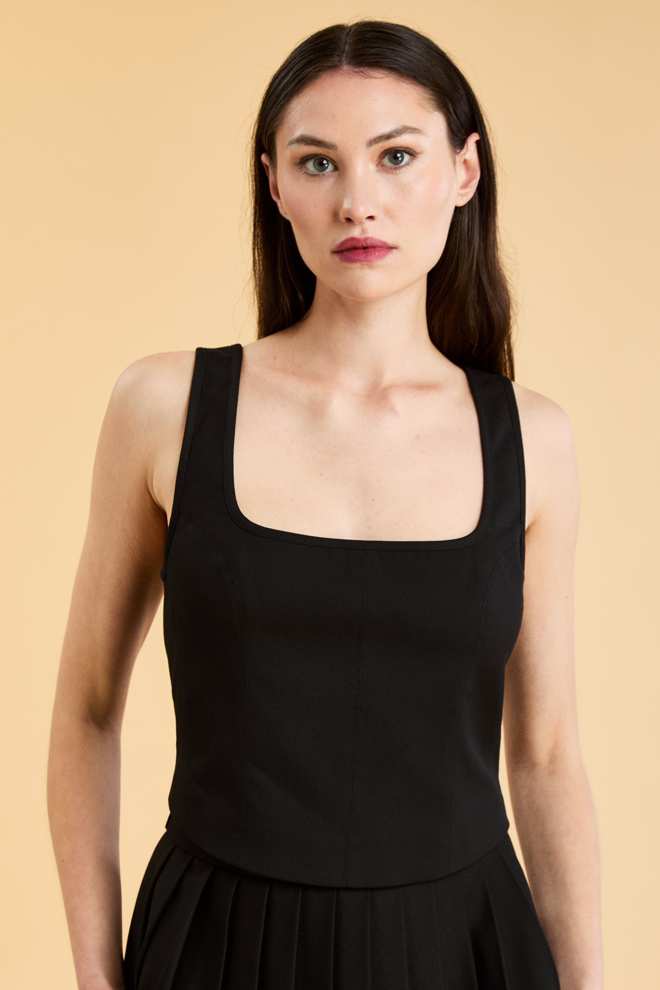 Woman wearing a Black Triplicity sleeveless Eloise tank up against a beige background front view close up