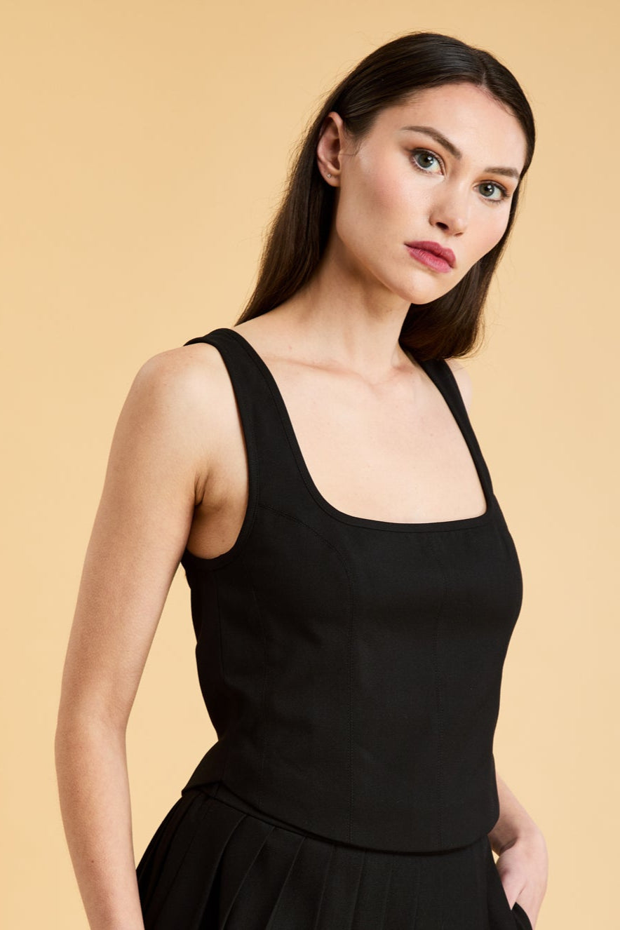 Woman wearing a Black Triplicity sleeveless Eloise tank up against a beige background front view close up