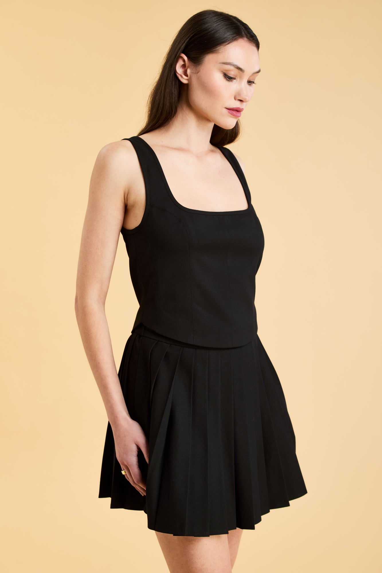 Woman wearing a Black Triplicity sleeveless Eloise tank up against a beige background three quarter view close up