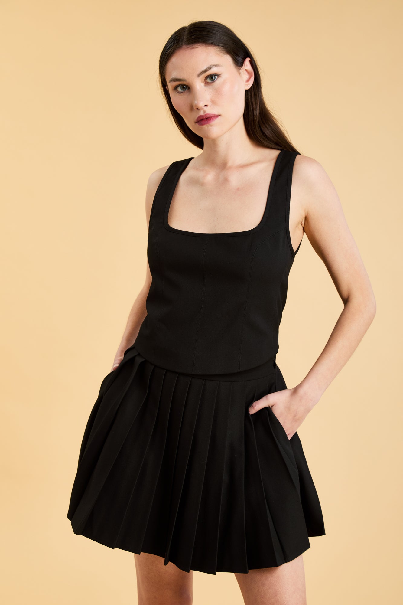 Woman wearing a Black Triplicity sleeveless Eloise tank up against a beige background front view close up