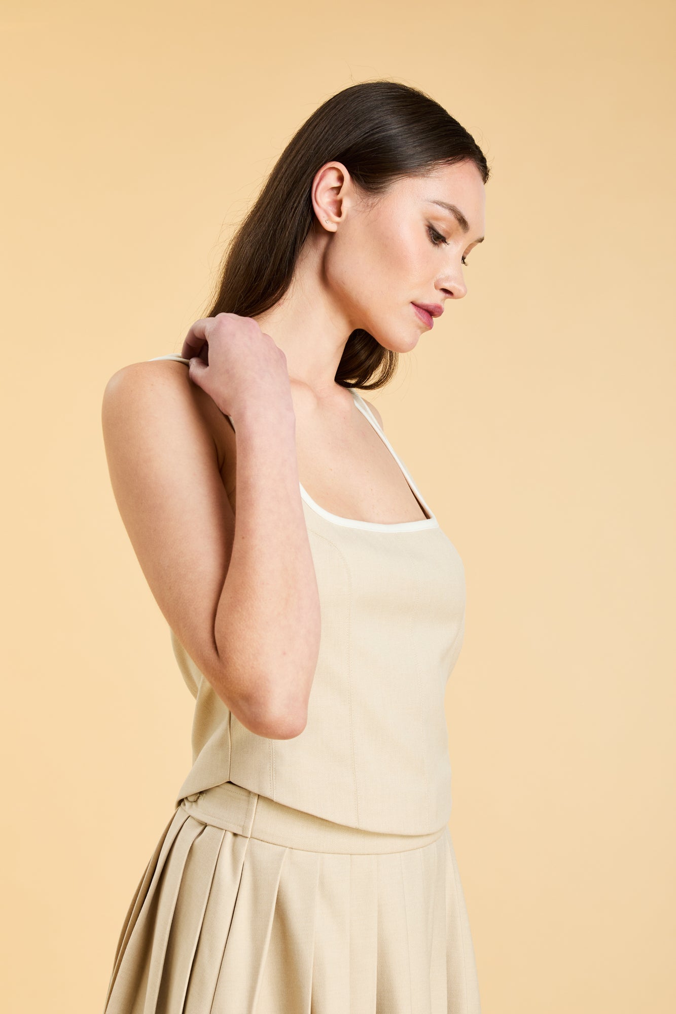 Woman wearing a Oat colored Triplicity Eloise Tank Top on a Oat colored Elisabeth pleated midi skirt against a beige background side view close up