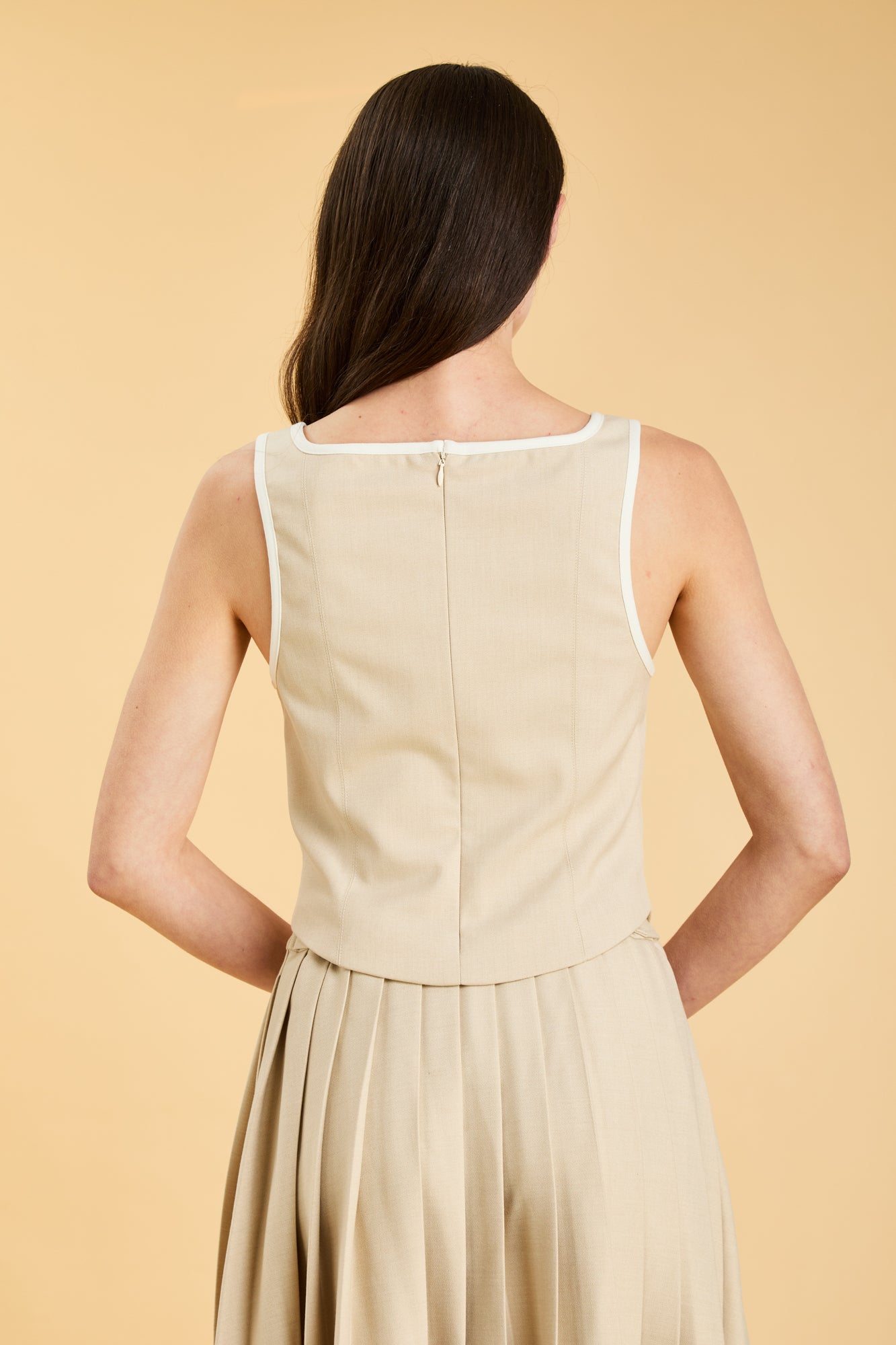Woman wearing a Oat colored Triplicity Eloise Tank Top on a Oat colored Elisabeth pleated midi skirt against a beige background