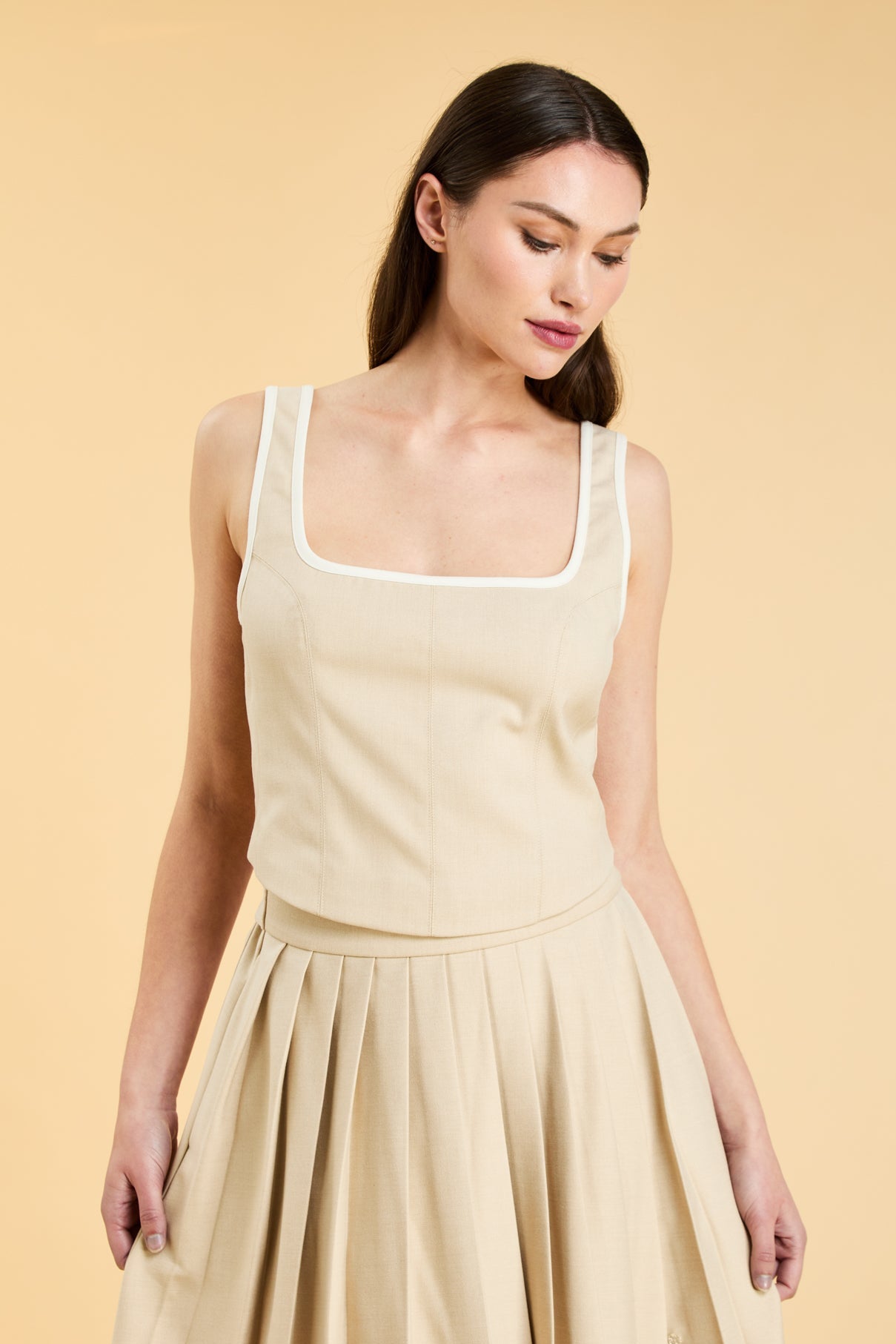 Woman wearing a Oat colored Triplicity Eloise Tank Top on a Oat colored Elisabeth pleated midi skirt against a beige background side view close up