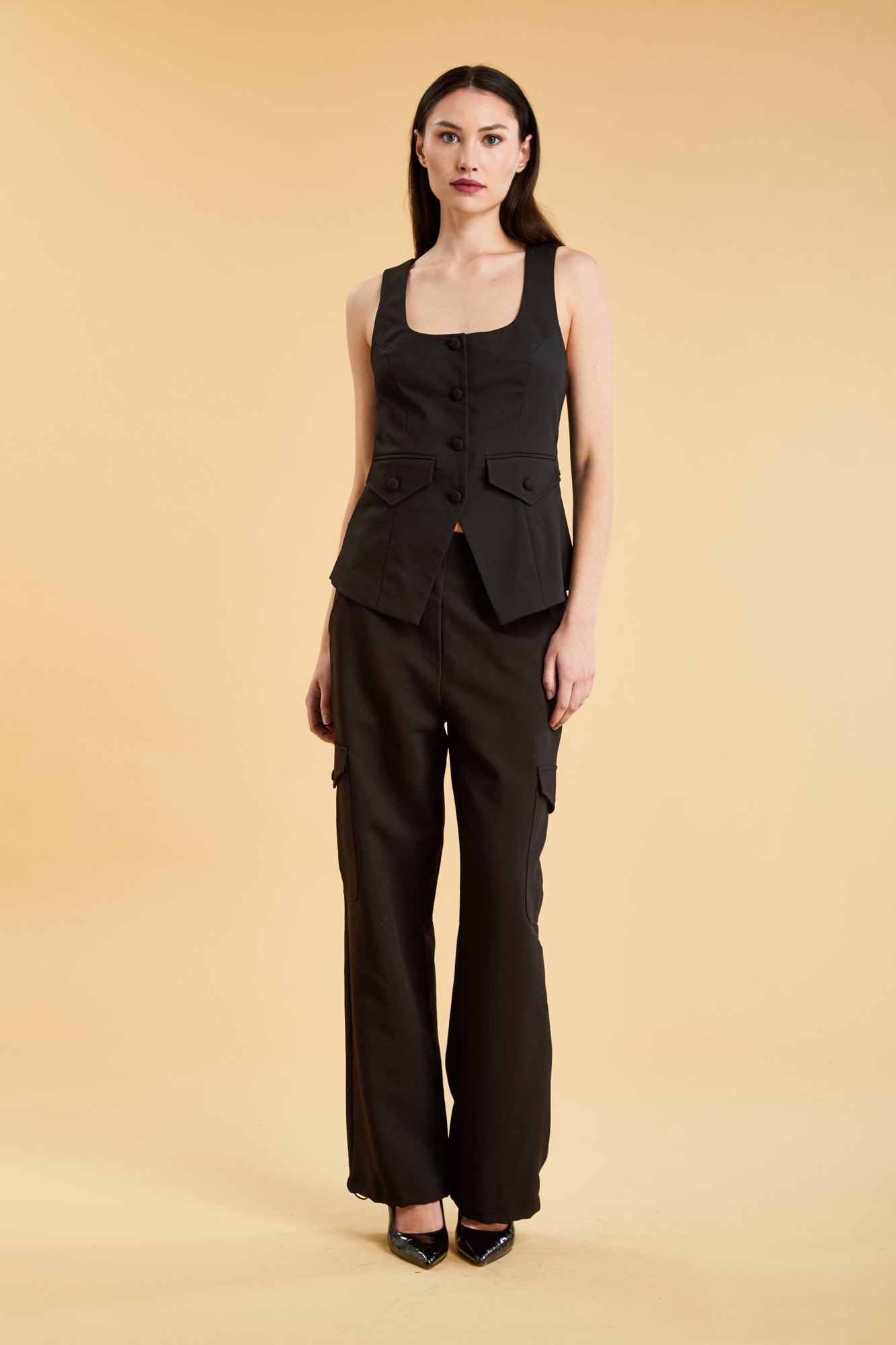 Woman wearing a Black Triplicity Georgiana Vest top on the Triplicity Triplicity Adelaide cargo pant on a beige background front view full body