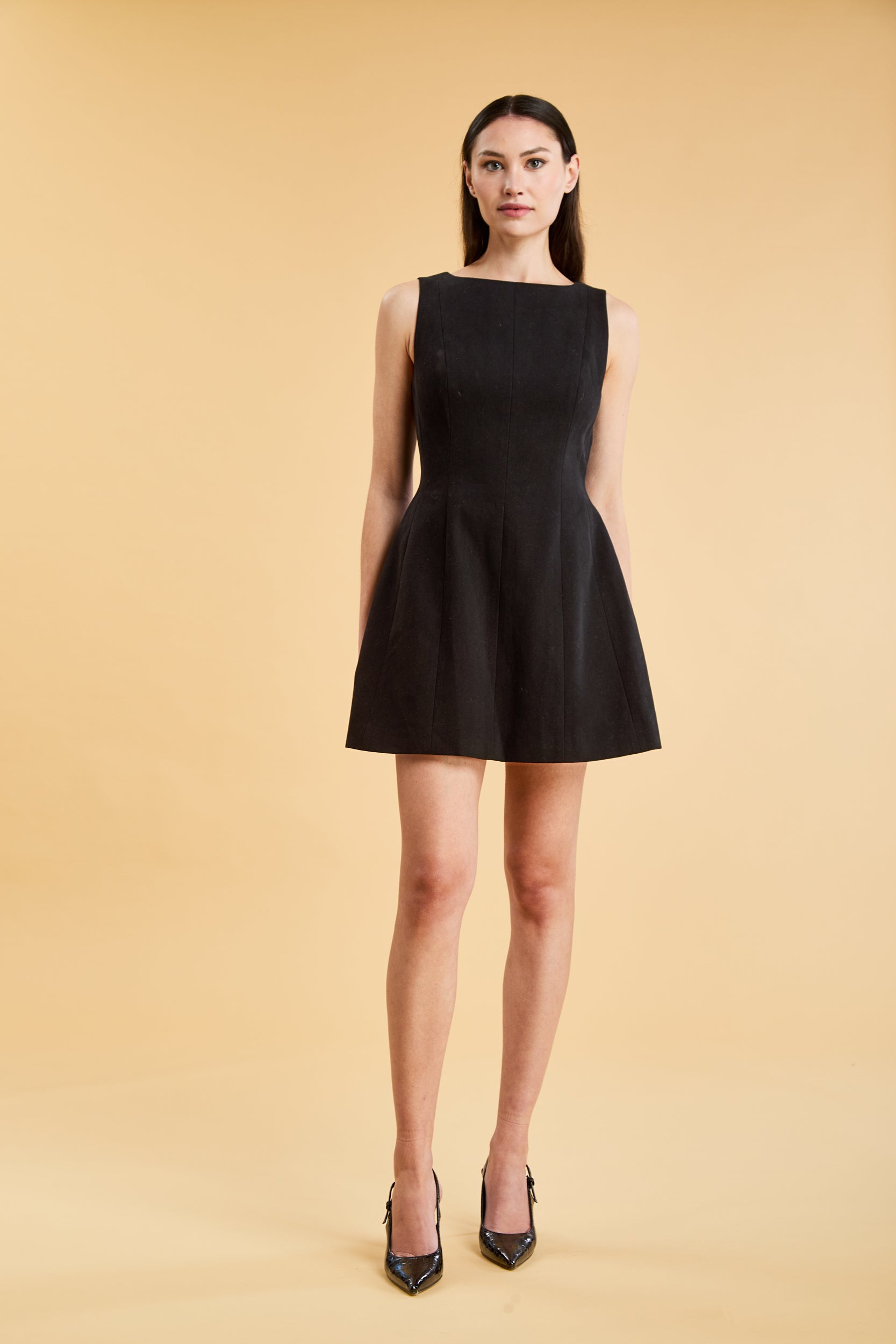 Full body view of a woman wearing the Triplicity Louise Sleeveless Mini Dress on a beige background
