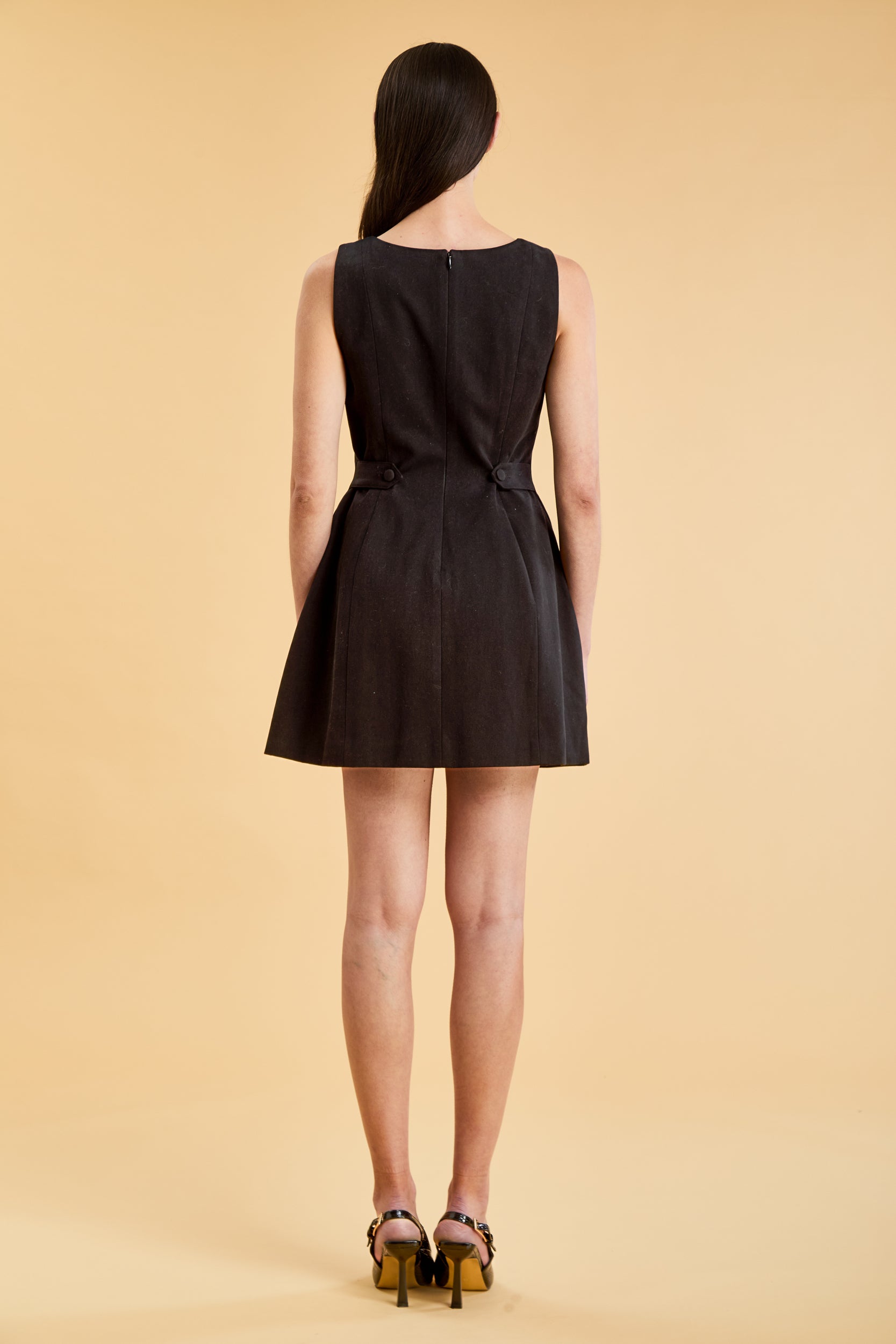 Full body view of a woman wearing the Triplicity Louise Sleeveless Mini Dress on a beige background