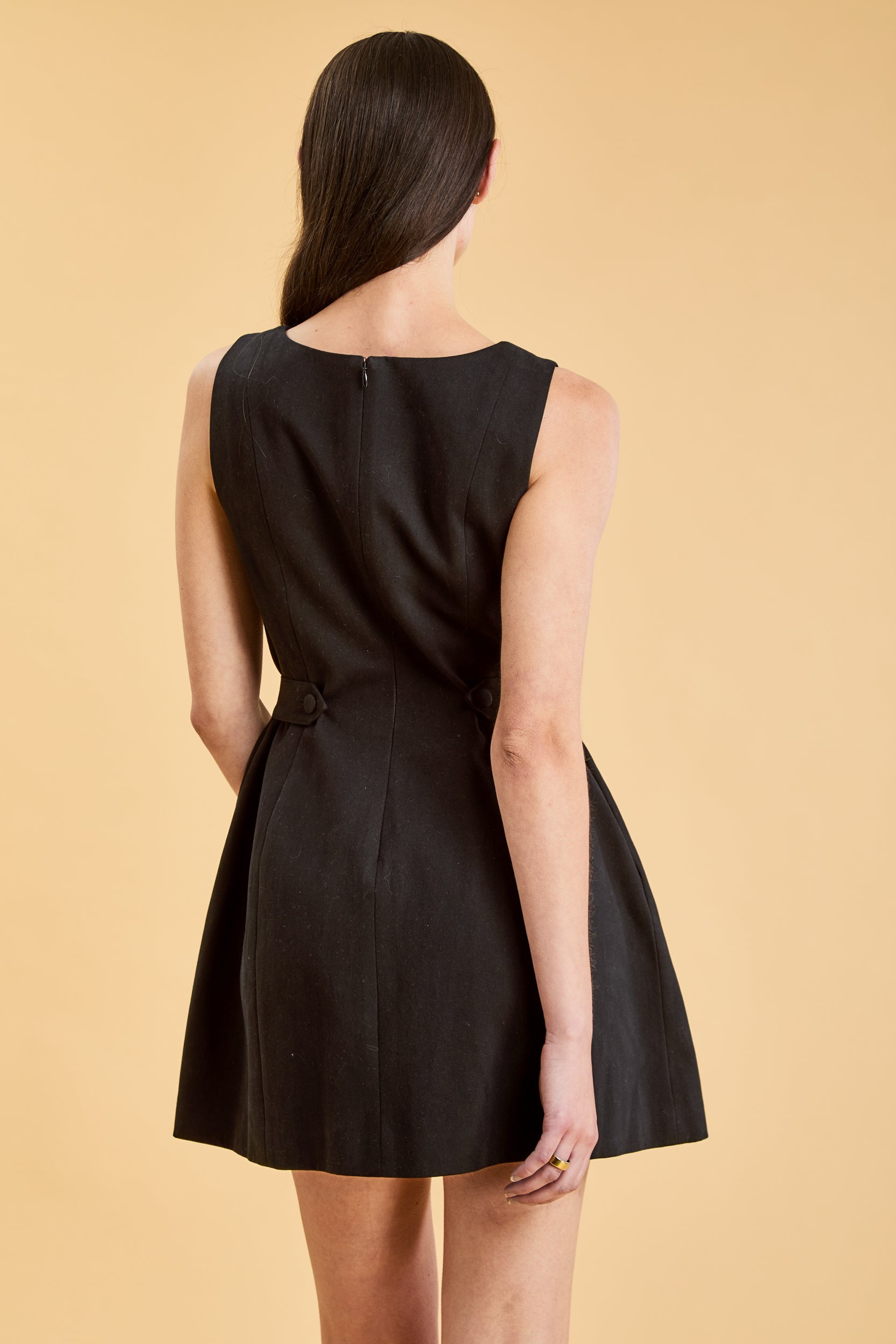 women from behind close up of her wearing the Triplicity Louise Sleeveless Mini Dress on a beige background