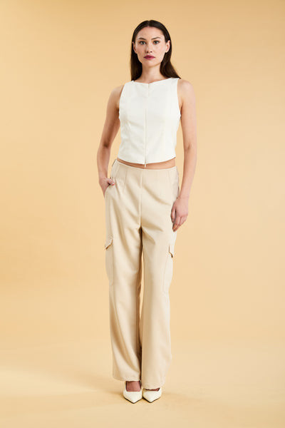 Woman wearing a white sleeveless double zipper top and beige almond Triplicity trousers cargo pants on a beige background