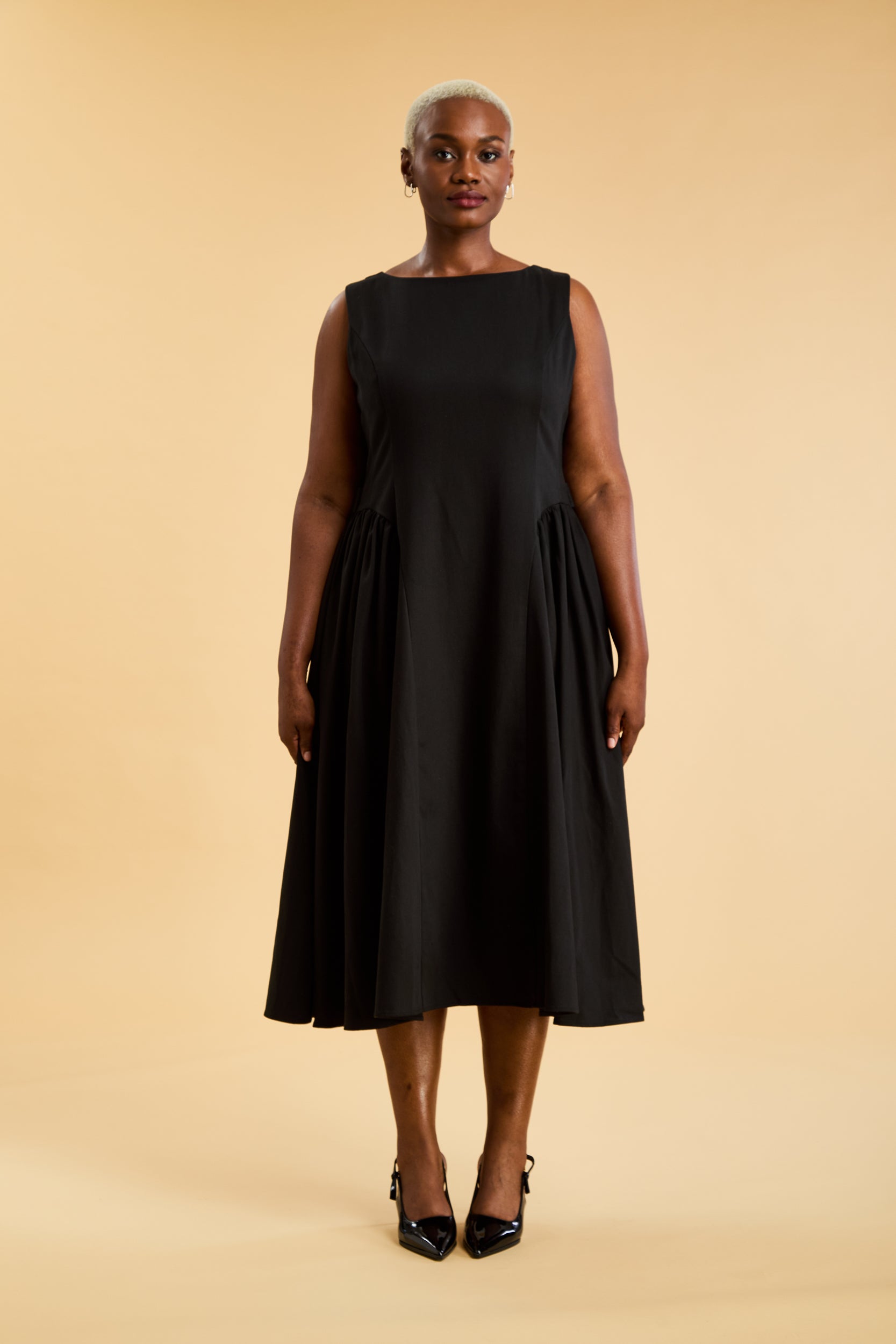 woman wearing a triplicity Black Eleanor Midi dress on a beige background