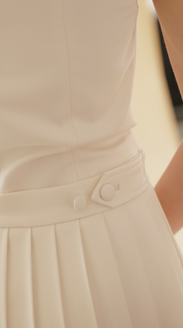 close up of the White Elisabeth pleated skirt adustable waist tab with hands tighening and loosening the buttons