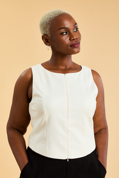 Woman wearing a white sleeveless top against a beige background