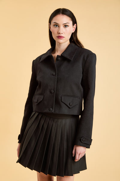 Woman wearing a Black Triplicity collared jacket and Black Triplicity pants on a beige background front close up