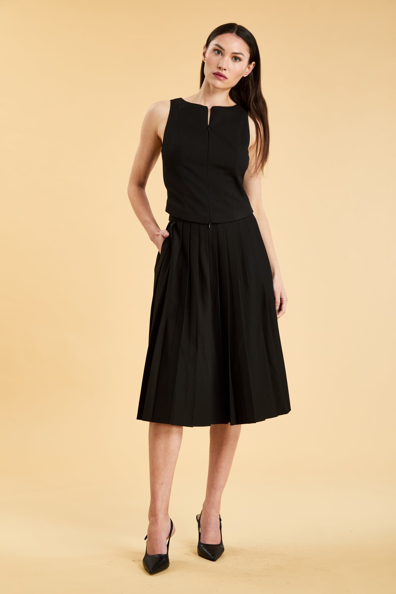 Woman wearing a black sleeveless top on a pleated Black midi skirt on a beige background