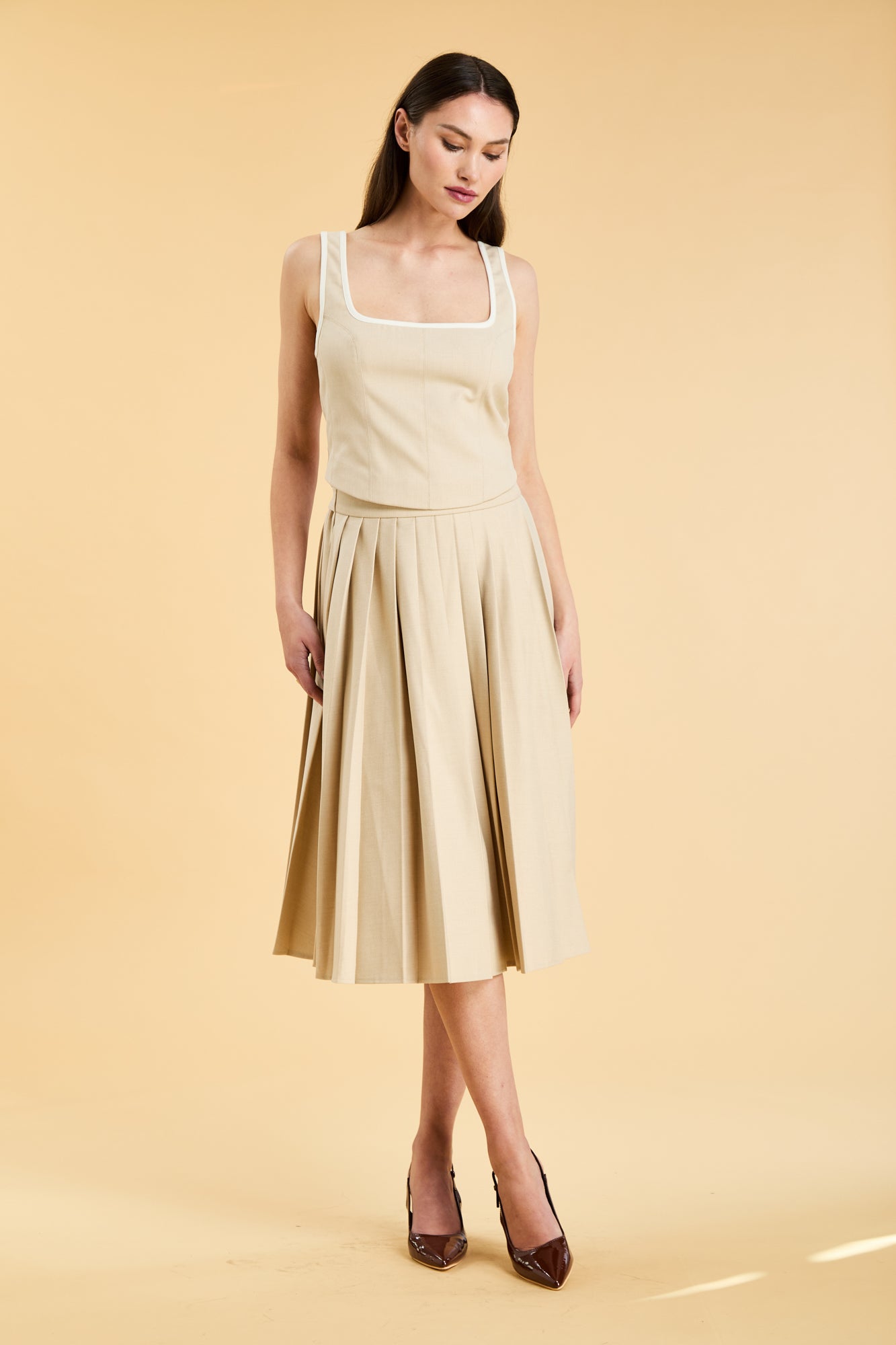 Woman wearing a beige sleeveless top and skirt on a yellow background