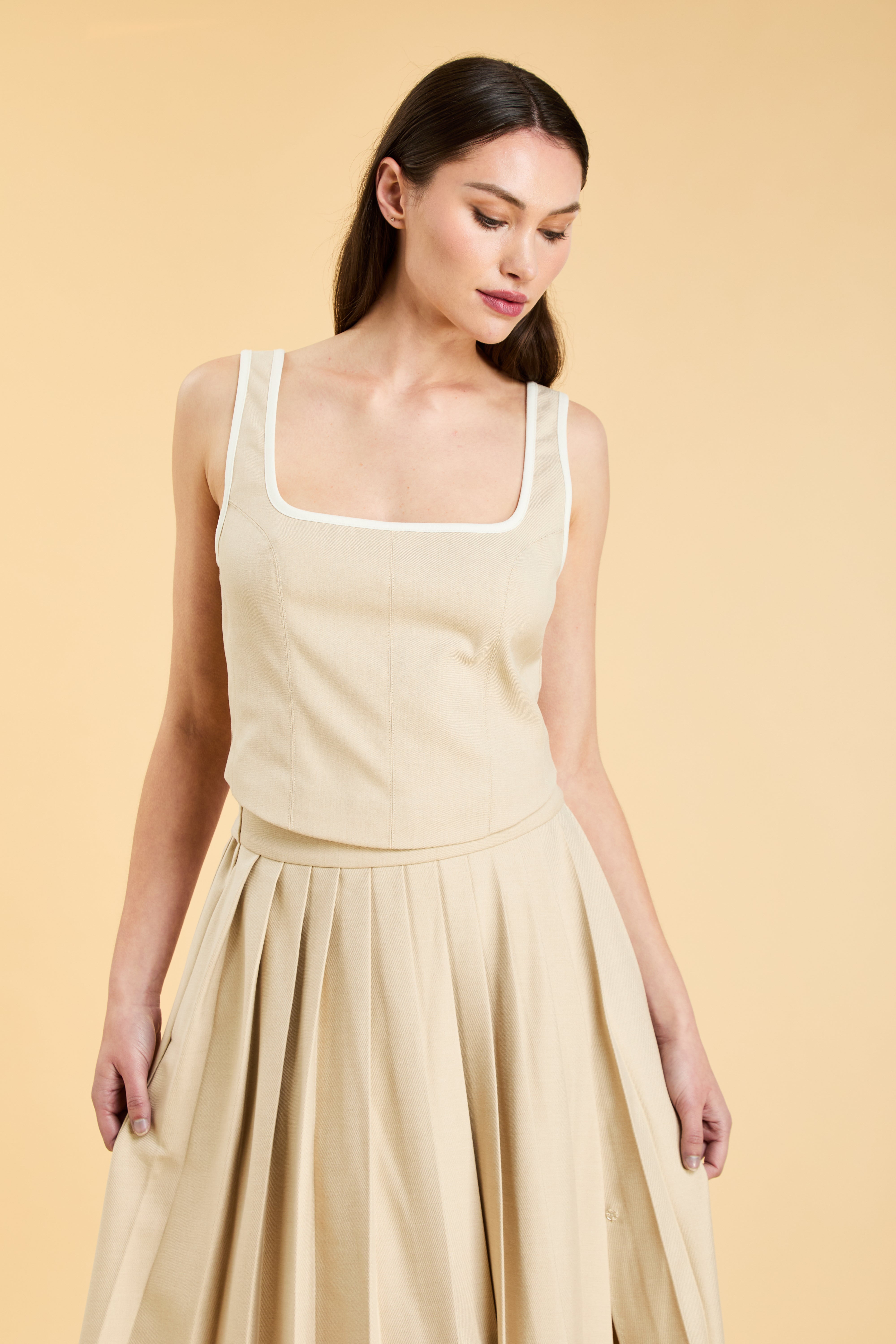 Woman wearing a Oat colored Triplicity Eloise Tank Top on a Oat colored Elisabeth pleated midi skirt against a beige background side view close up