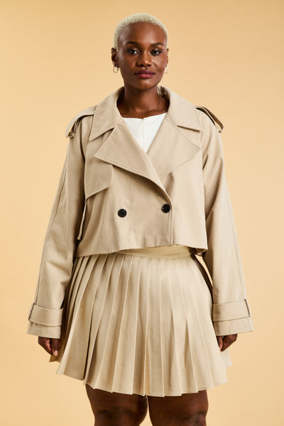 Woman wearing a beige cropped trench coat jacket in stone color against a beige background