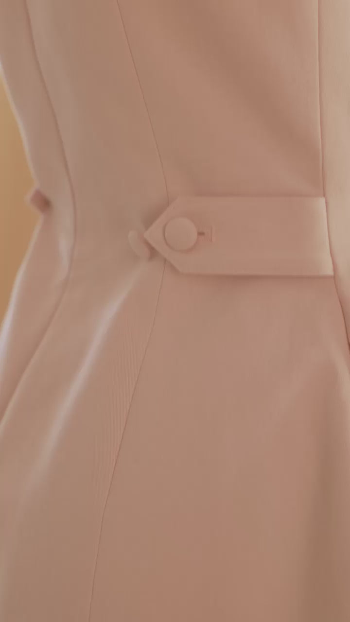close up of hands buttoning the waist adjustable tabs on the Blush pink Louise mini dress to tighten the waist