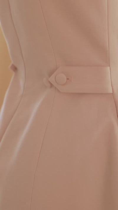 close up of hands buttoning the waist adjustable tabs on the Blush pink Louise mini dress to tighten the waist
