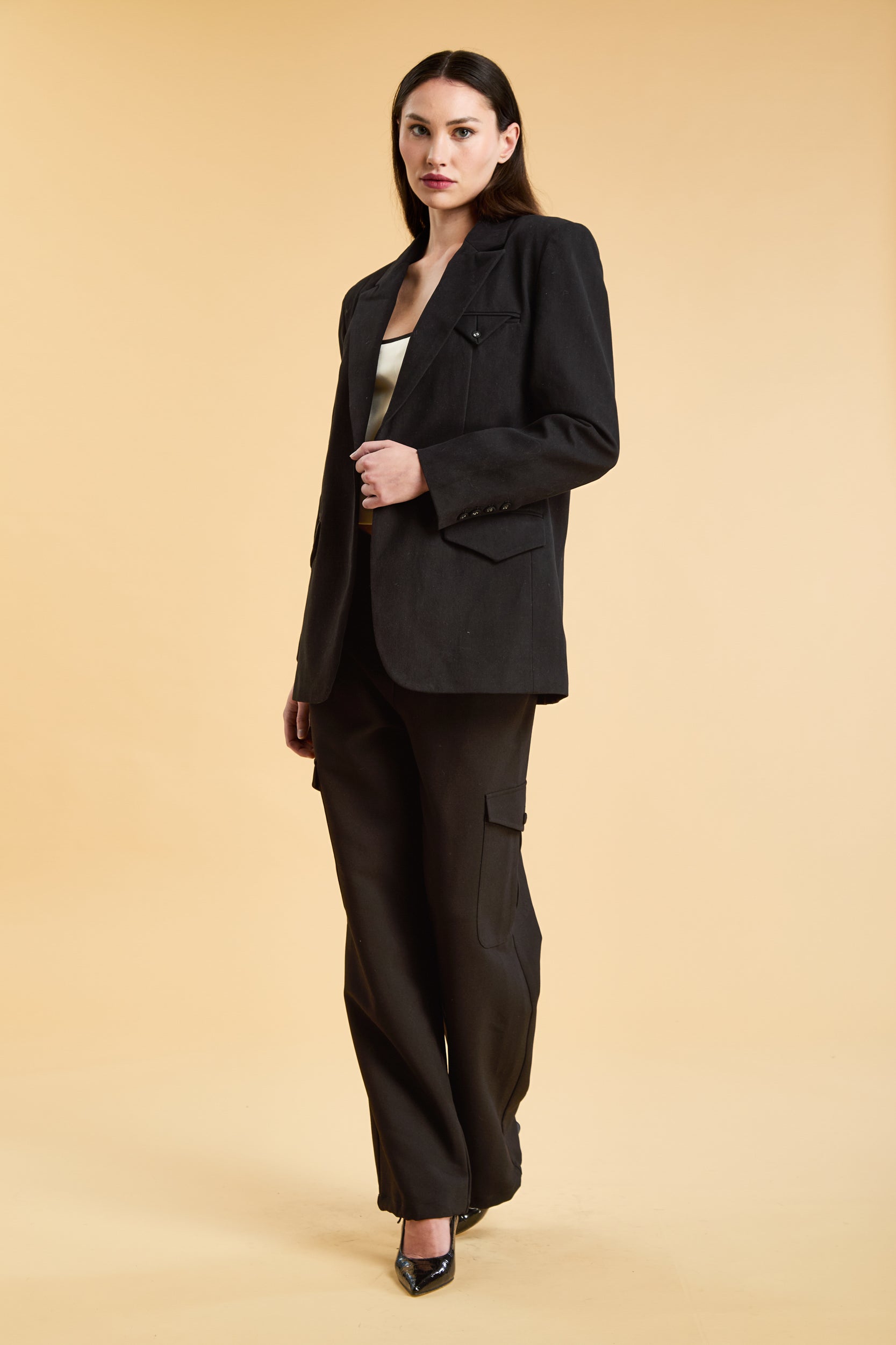Woman wearing a Black oversized triplicity blazer over a white top on a beige background front view full body