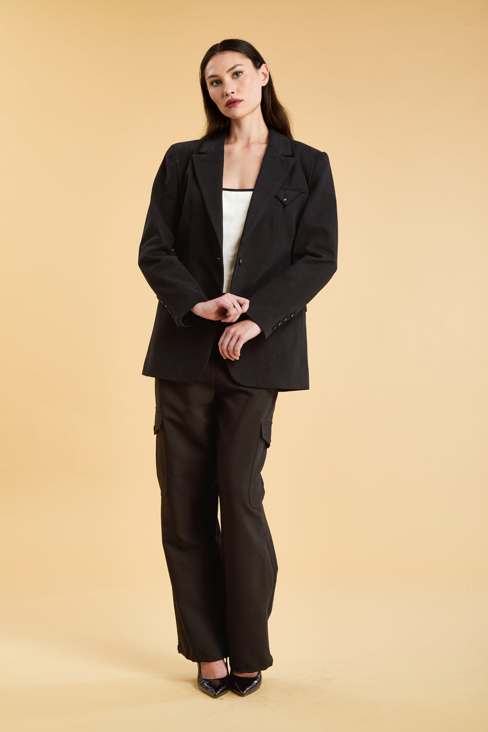 Woman wearing a Black oversized triplicity blazer over a white top on a beige background front view full body