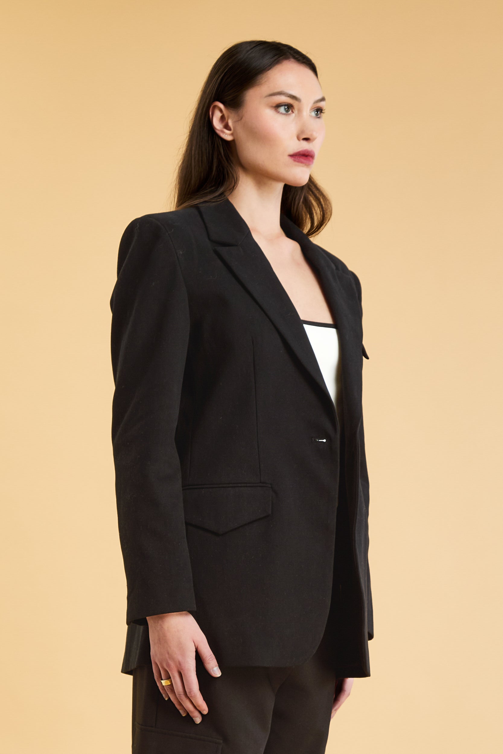 Woman wearing a Black oversized triplicity blazer over a white top on a beige background three quarter view cropped