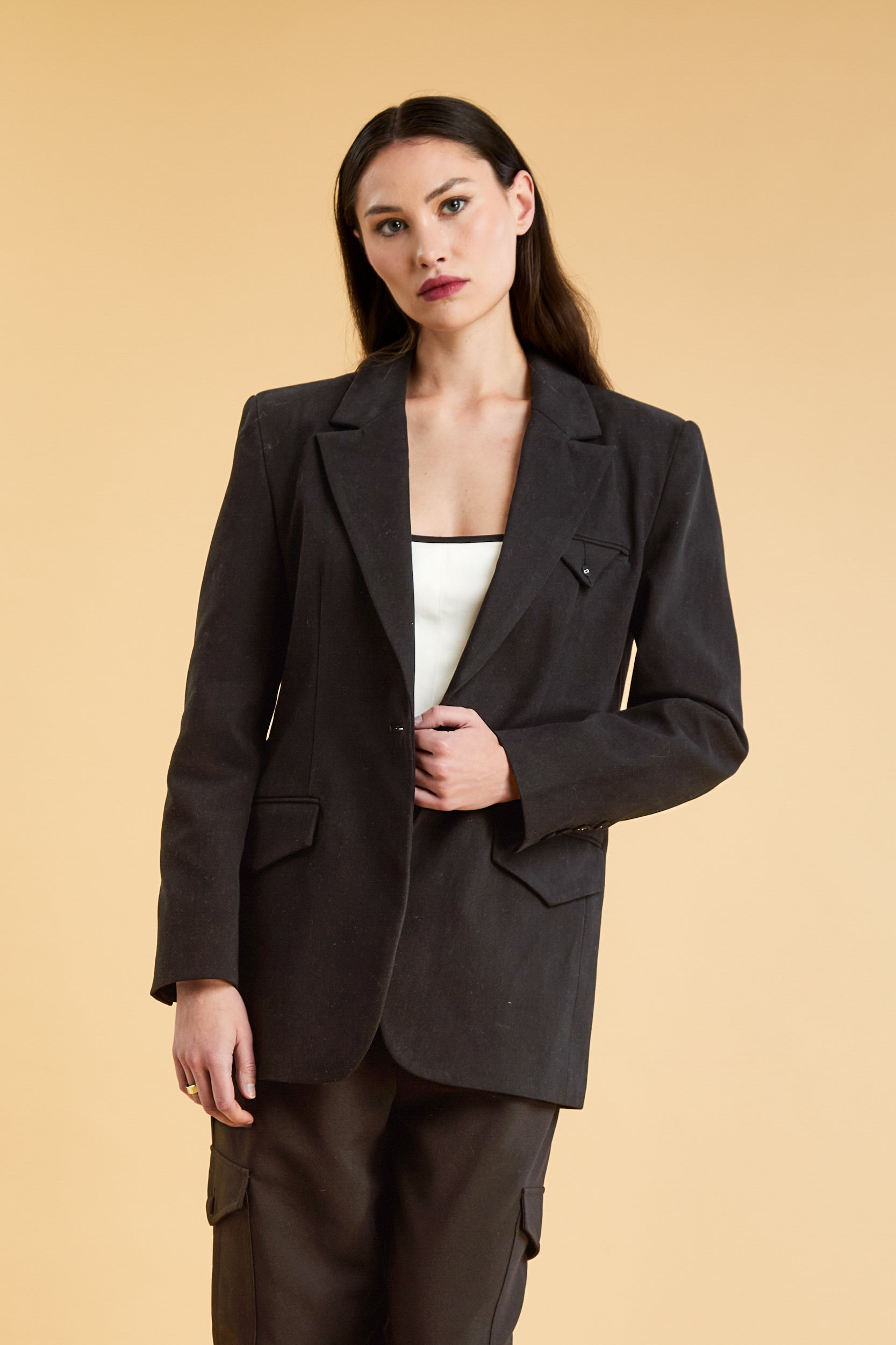 Woman wearing a Black oversized triplicity blazer over a white top on a beige background front view cropped
