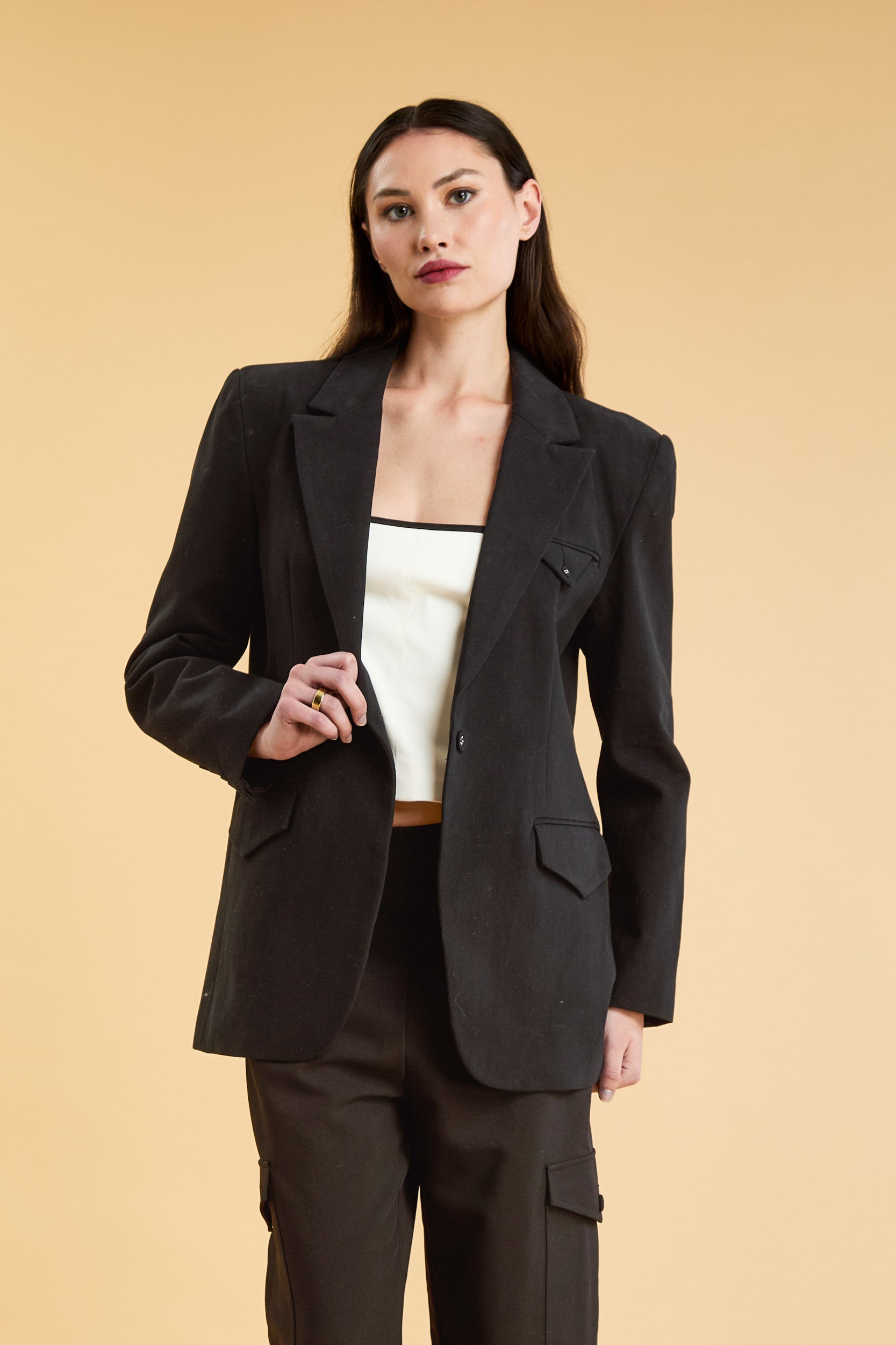 Woman wearing a Black oversized triplicity blazer over a white top on a beige background front view cropped