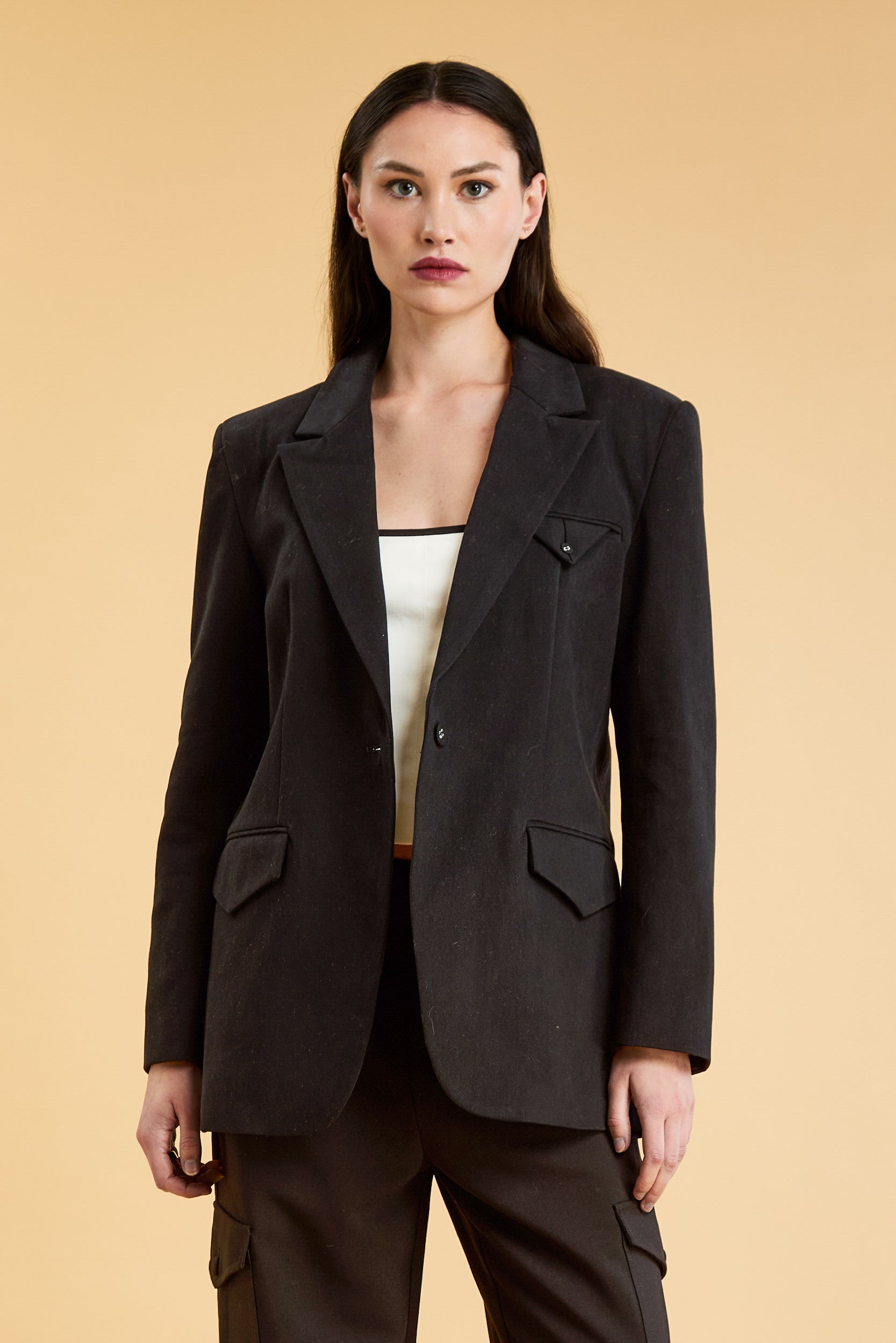 Woman wearing a Black oversized triplicity blazer over a white top on a beige background front view cropped