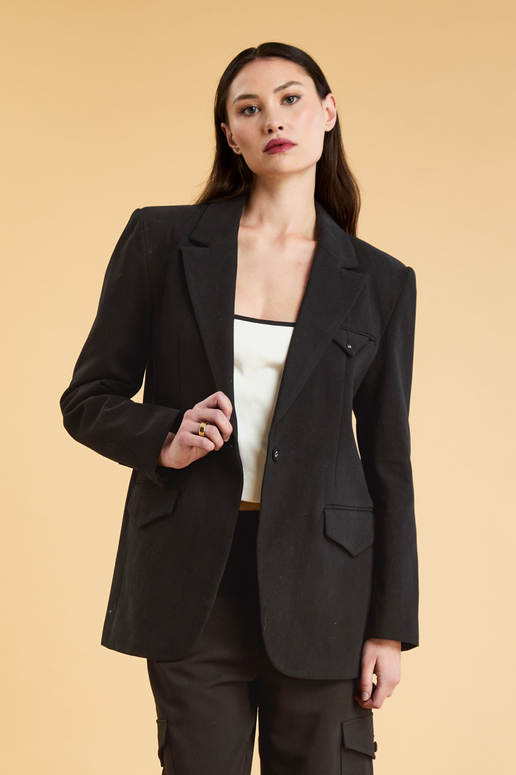 Woman wearing a Black oversized triplicity blazer over a white top on a beige background front view cropped