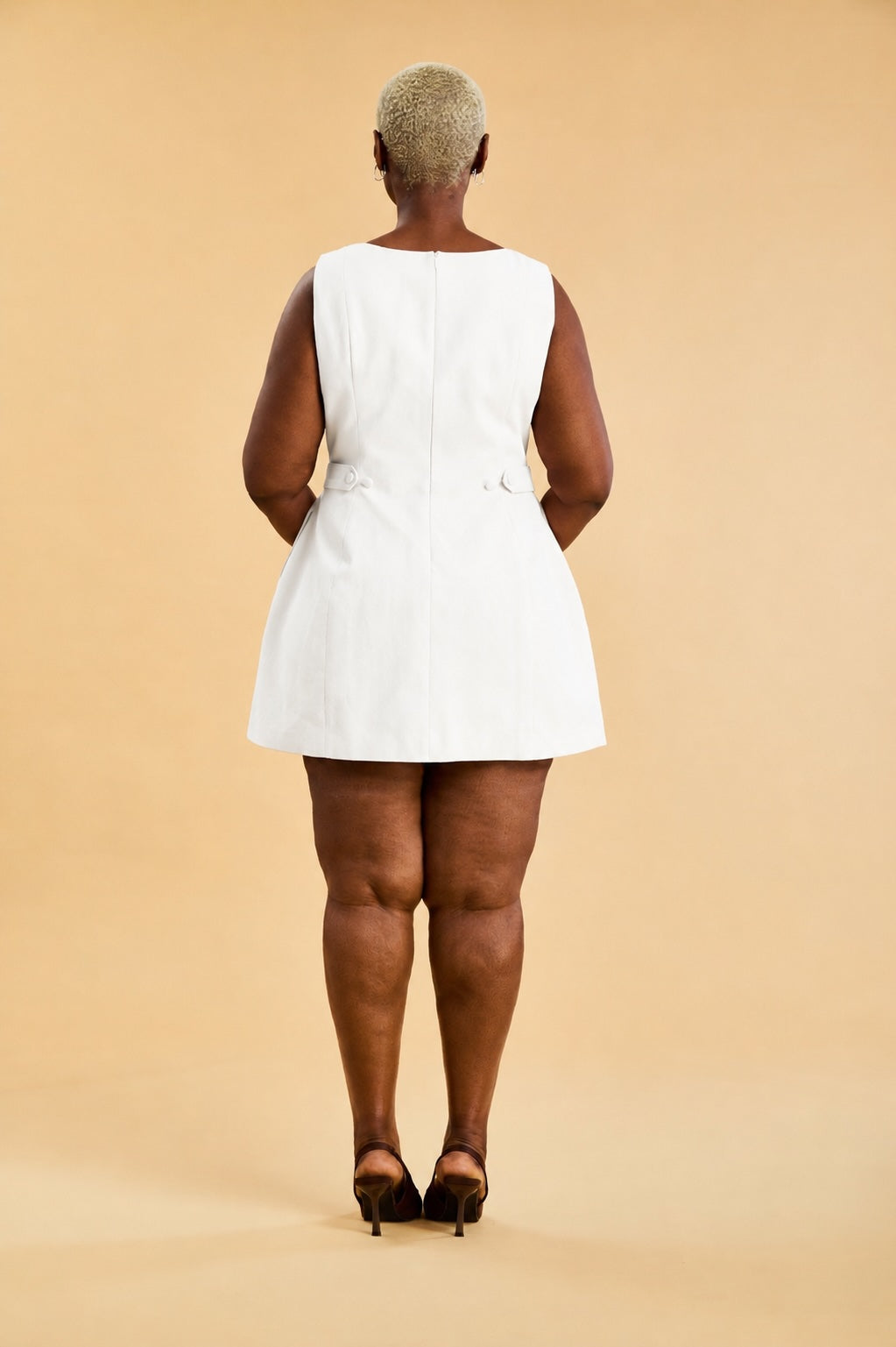 Person wearing a white dress standing against a beige background